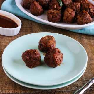 Completed Instant Pot Orange BBQ Meatballs in an oval serving platter with three meatballs on a white plate set in front