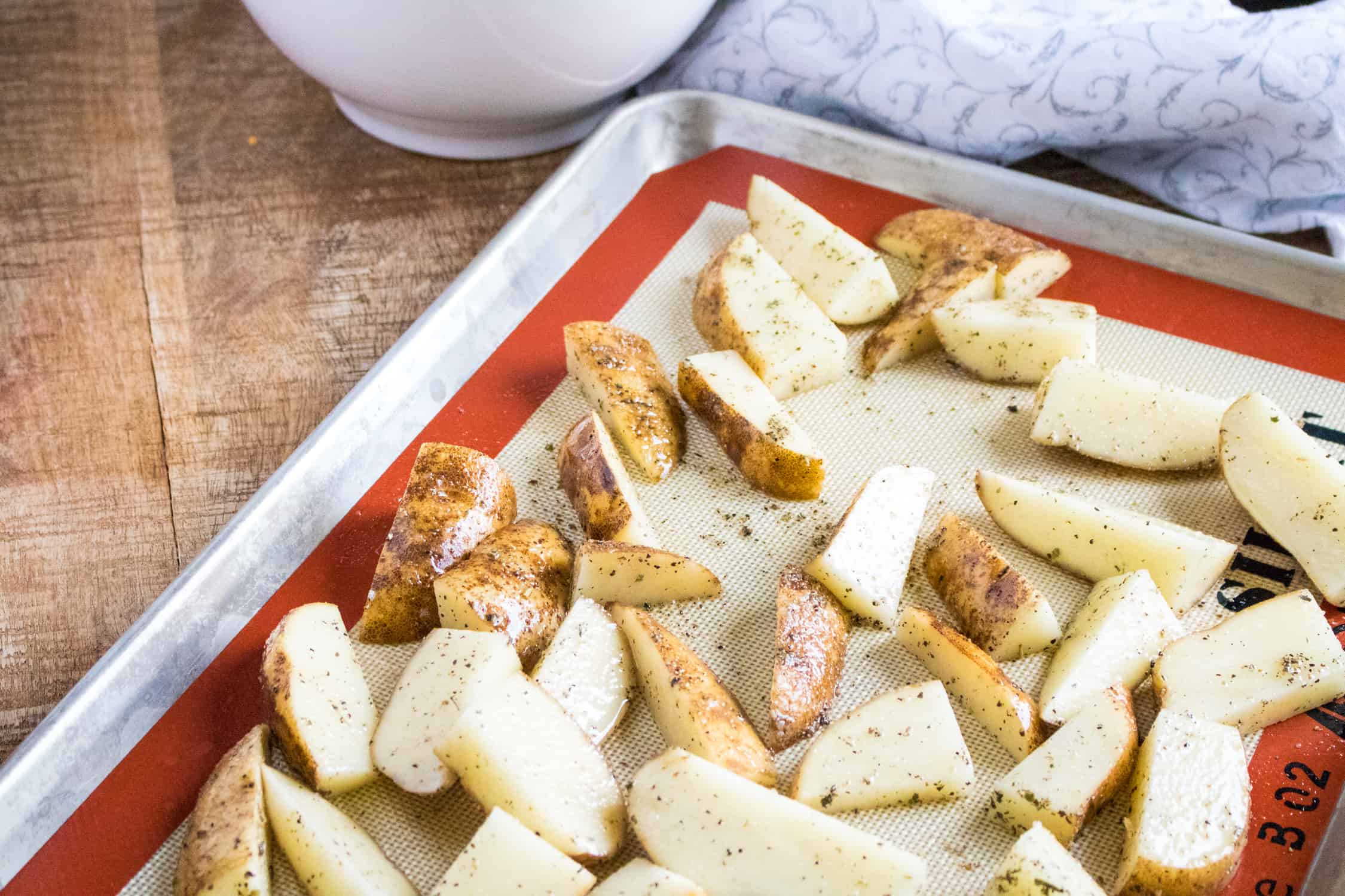 chunks of seasoned potatoes spread out on a baking sheet lined with silicone baking mat