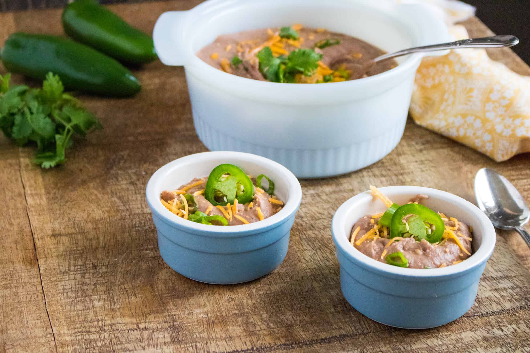 Instant Pot Refried Beans served in two blue bowls and garnished with grated cheese, sliced peppers and cliantro