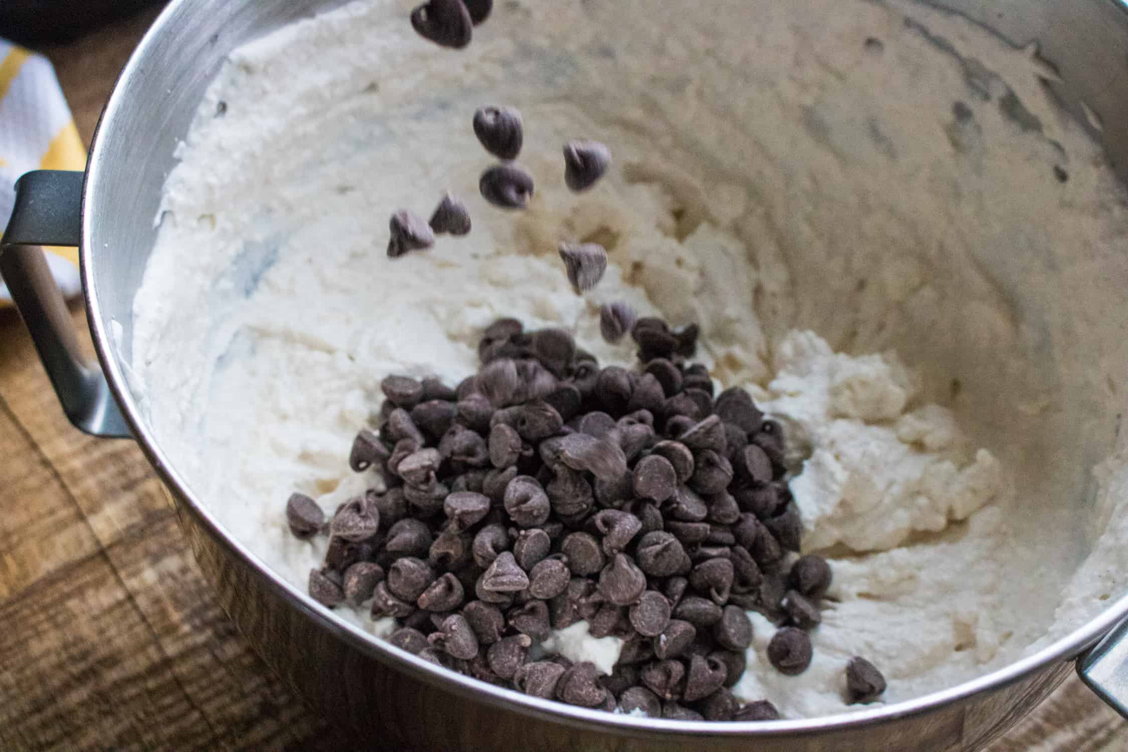 silver mixing bowl with cannoli cream cake roll filling in it with chocolate chips added but not mixed in