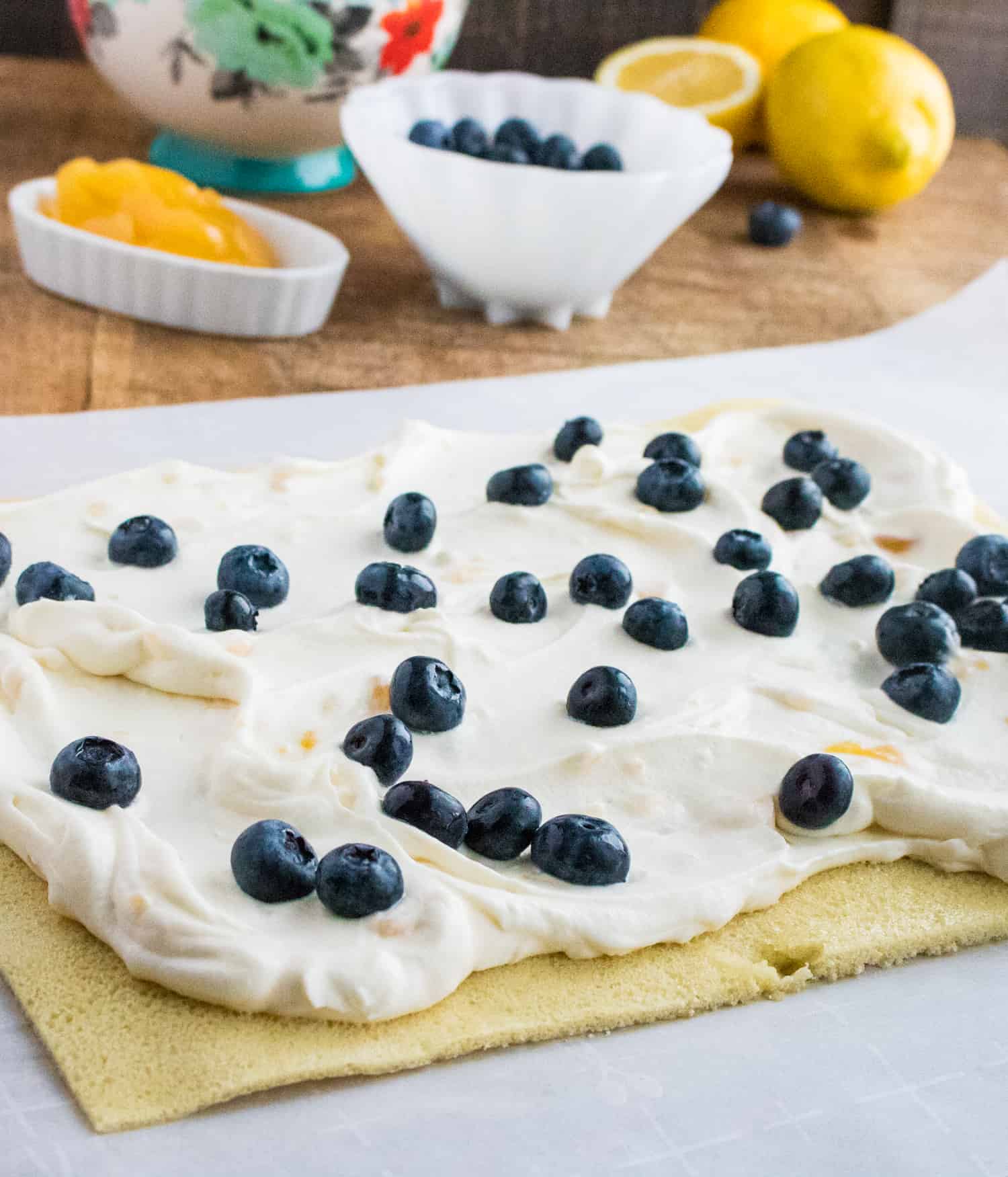 cake roll dough rolled flat covered in lemon cream and sprinkled with blueberries