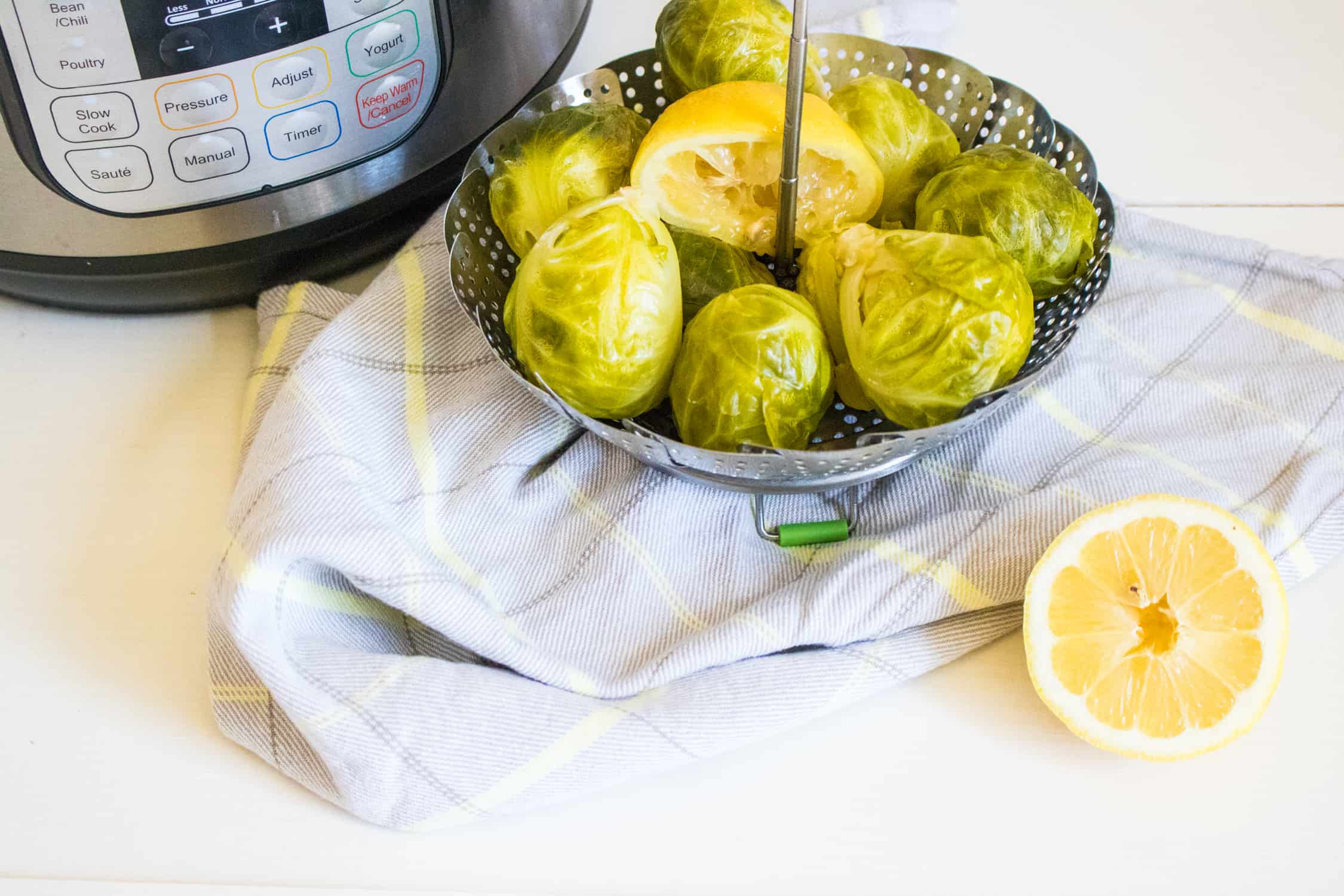 close-up of steamer basket filled with Brussels sprouts and half squeezed lemon set on top of a pale blue and yellow plaid napkin
