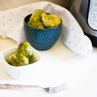 Instant Pot Lemon Pepper Brussels Sprouts served in white and blue bowls next to a polka dot cloth napkin, silver folk, and whole lemon