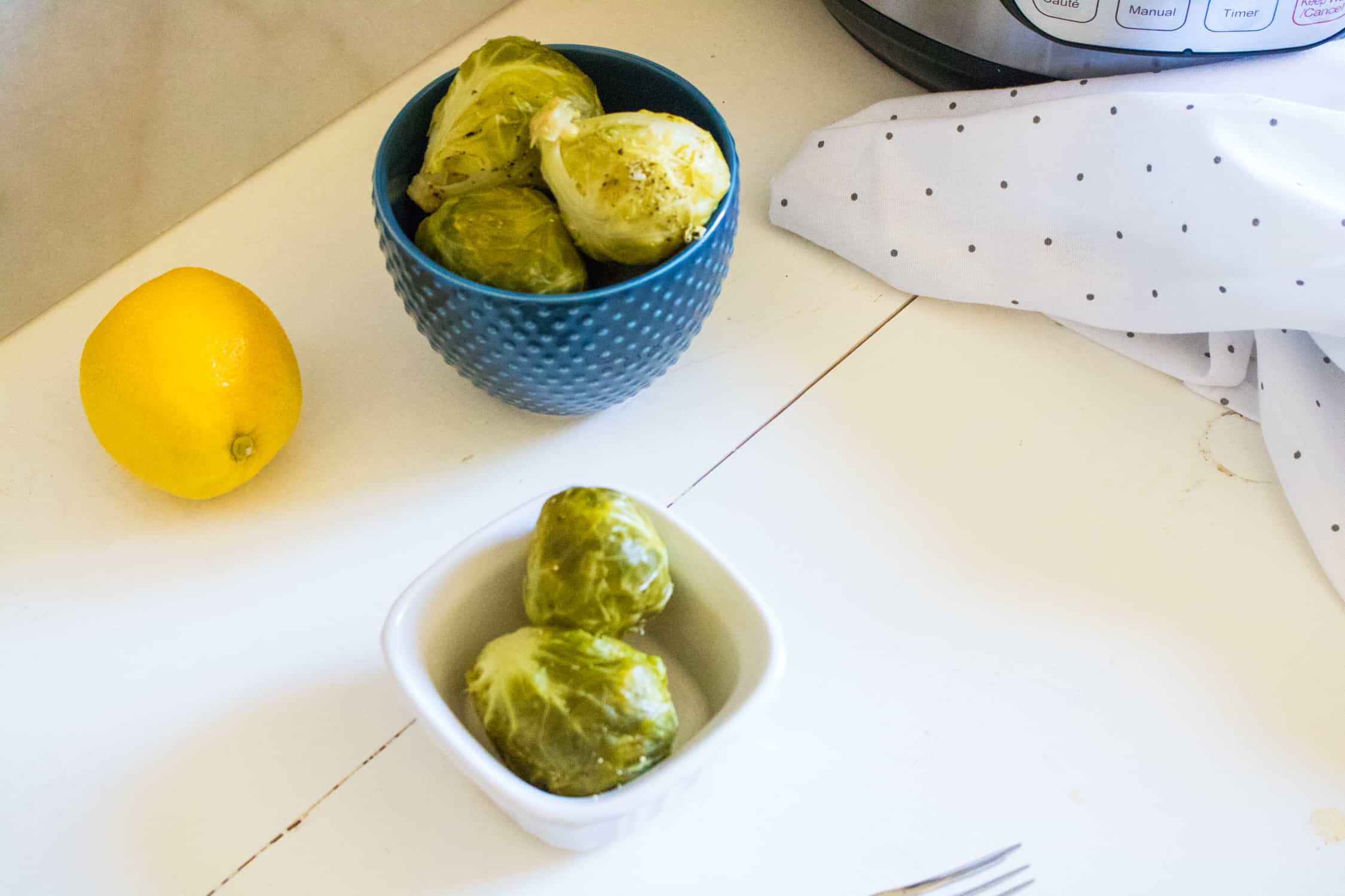 two bowls of instant pot lemon pepper brussels sprouts next to a whole lemon, polka dot cloth napkin