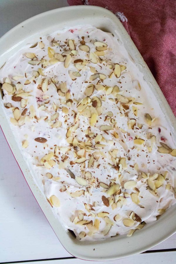 Finished cherry almond poke cake with whipped topping and sliced almonds