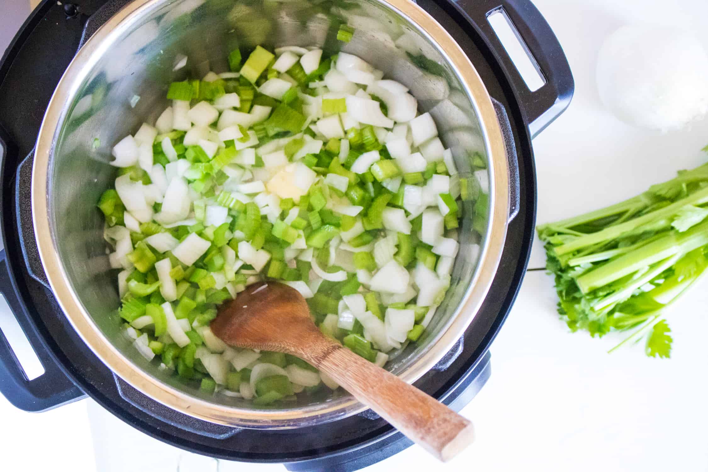 top-down view of diced onions and celery inside the instant pot being stirred by a wooden spoon