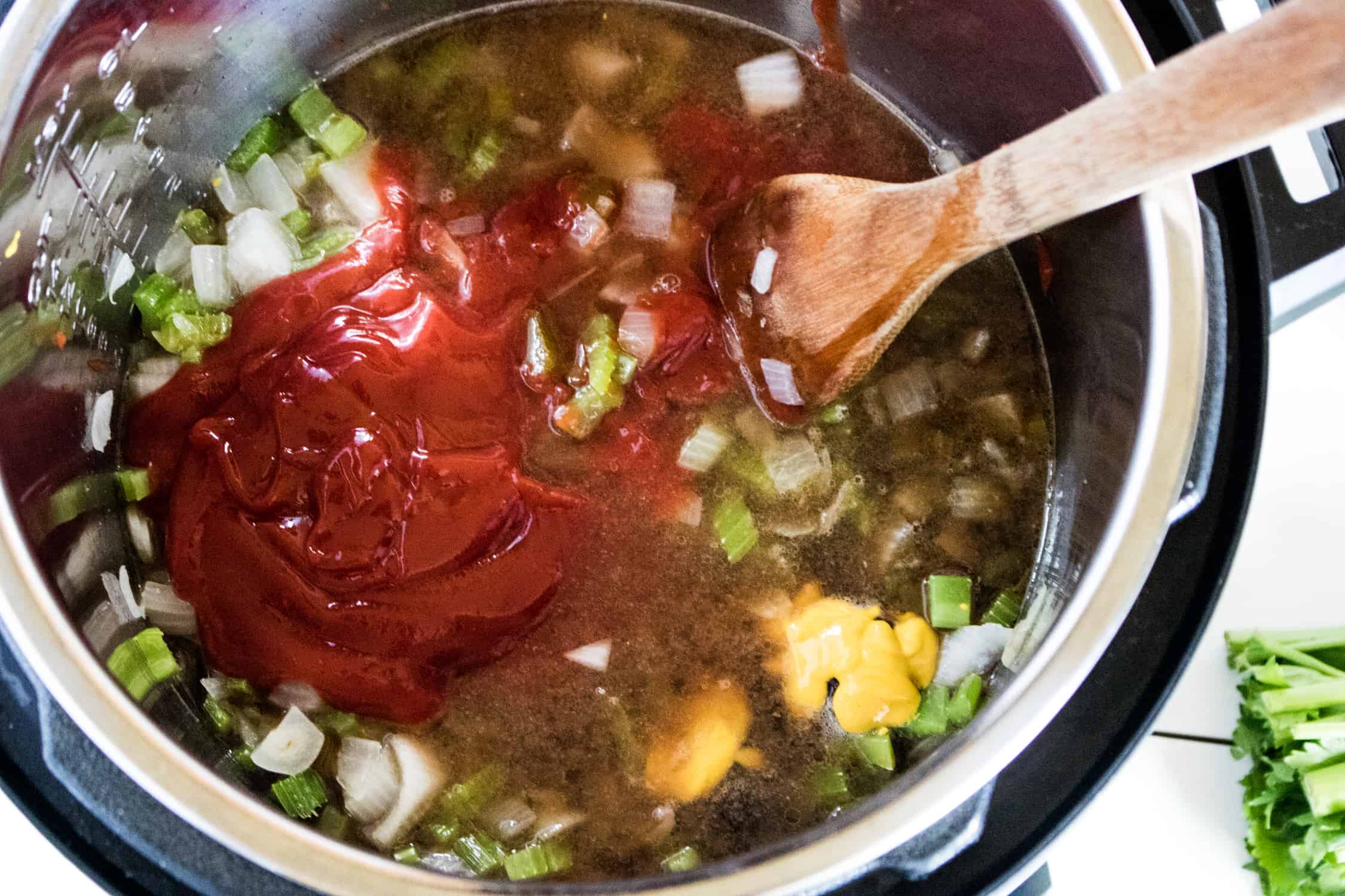 close-up of all ingredients for Instant Pot BBQ Sauce Recipe inside the Instant Pot and being stirred with a wooden spoon