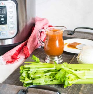 Completd Instant Pot BBQ Sauce in a glass pitcher on a wooden serving tray next to celery, onion and a BBQ sauce brush