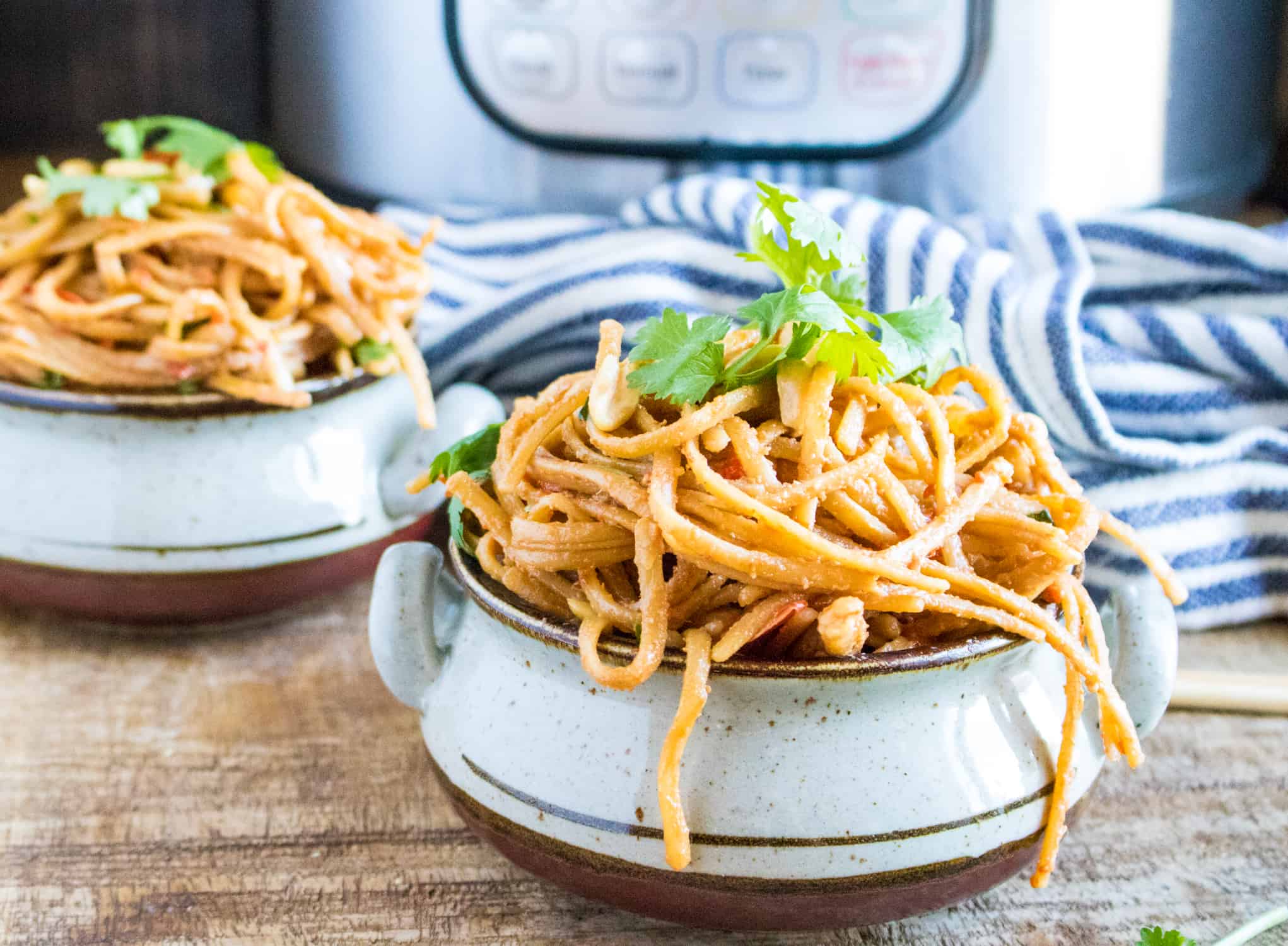 two brown and white ceramic bowls filled with Instant Pot Thai Peanut Noodles garnished with cilantro