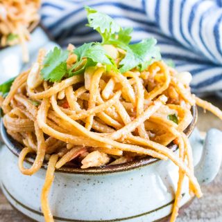 Instant Pot Thai Peanut Noodles served in a ceramic bowl next to a blue striped cloth napkin