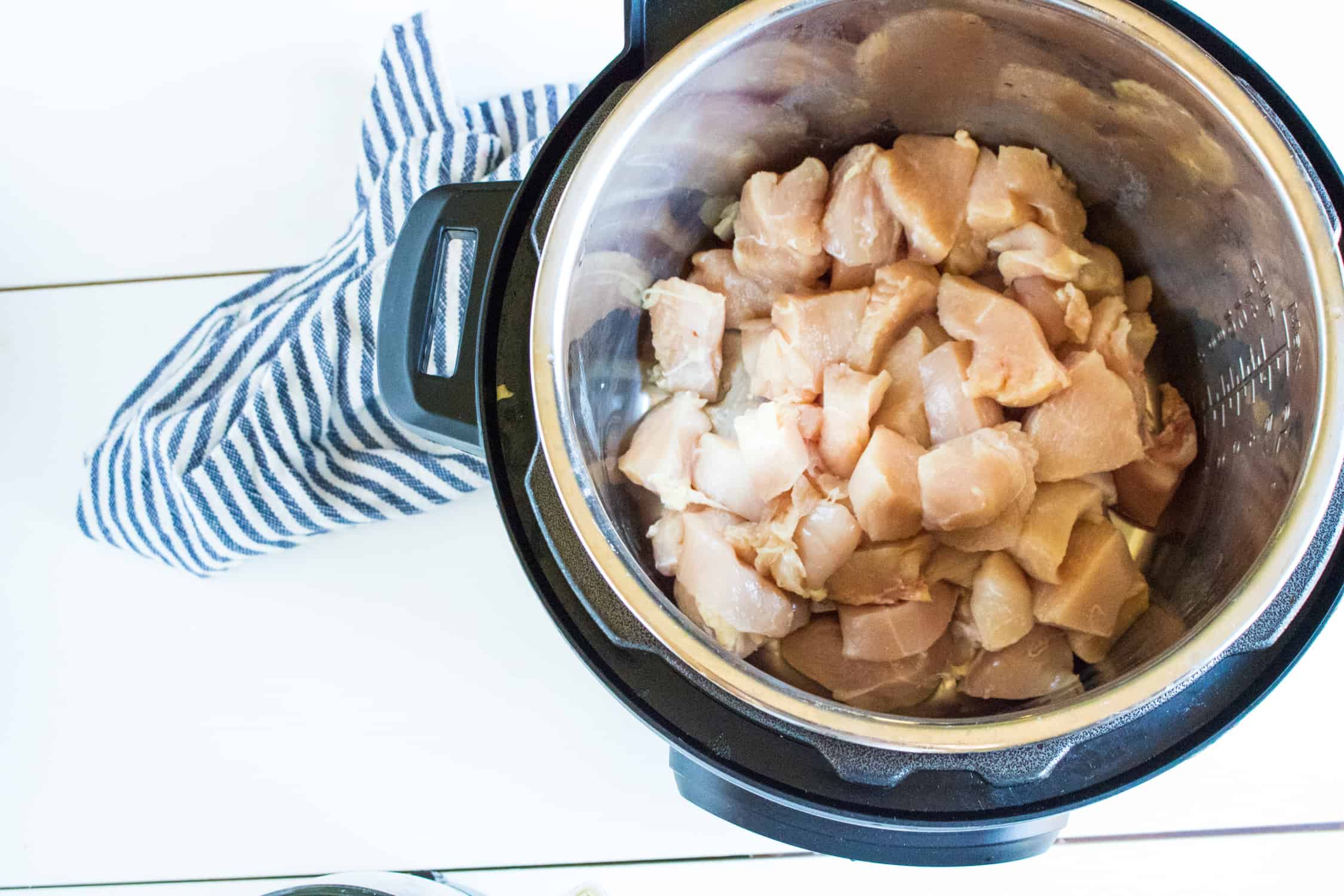 top-down view of the cut up chicken placed inside the Instant Pot, placed next to a blue striped kitchen towel