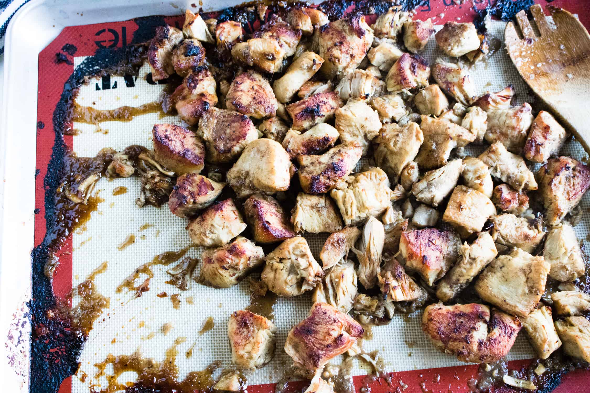cooked chicken spread out on a baking sheet lined with a non-stick silicone baking mat with the jerk sauce poured on top