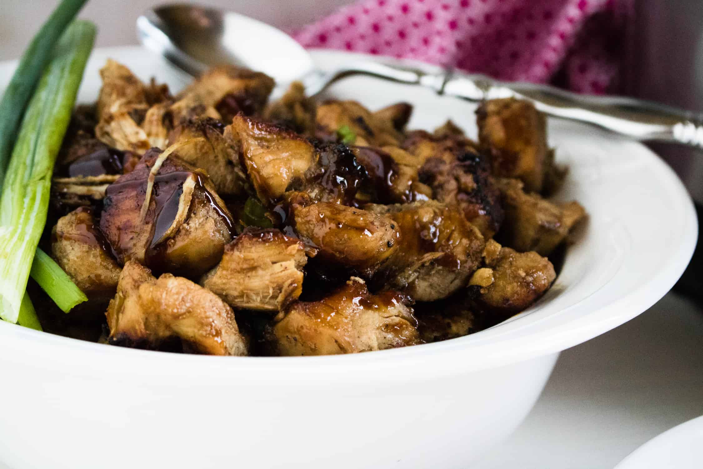 Close-up of the completed Instant Pot Jerk Chicken Recipe in a white serving bowl with silver serving spoon, sitting in front of a red print napkin