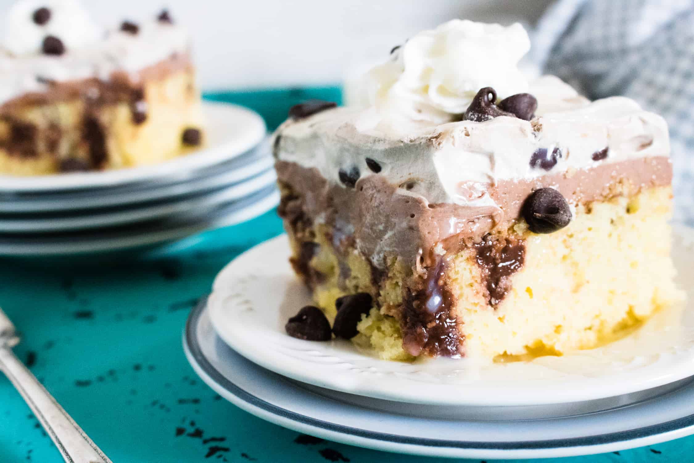 Slice of quadruple chocolate poke cake with chocolate pudding stripes, chocolate frosting and whipped topping on a white plate