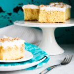 Caramel Toffee Poke Cake on a white cake stand next to a slice served on a blue dessert plate