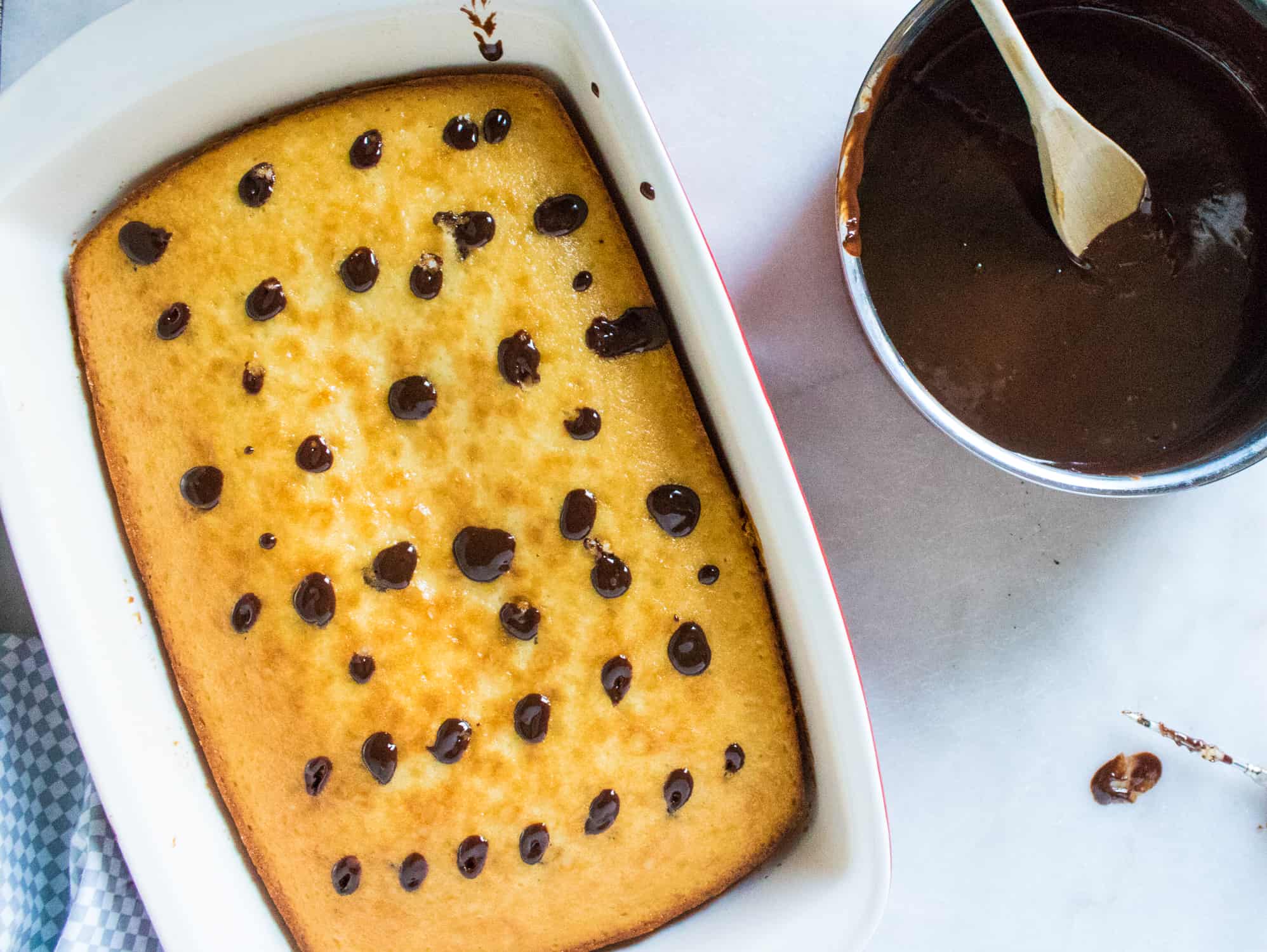 top-down view of the filled poke cake sitting next to a silver mixing bowl full of chocolate ganache