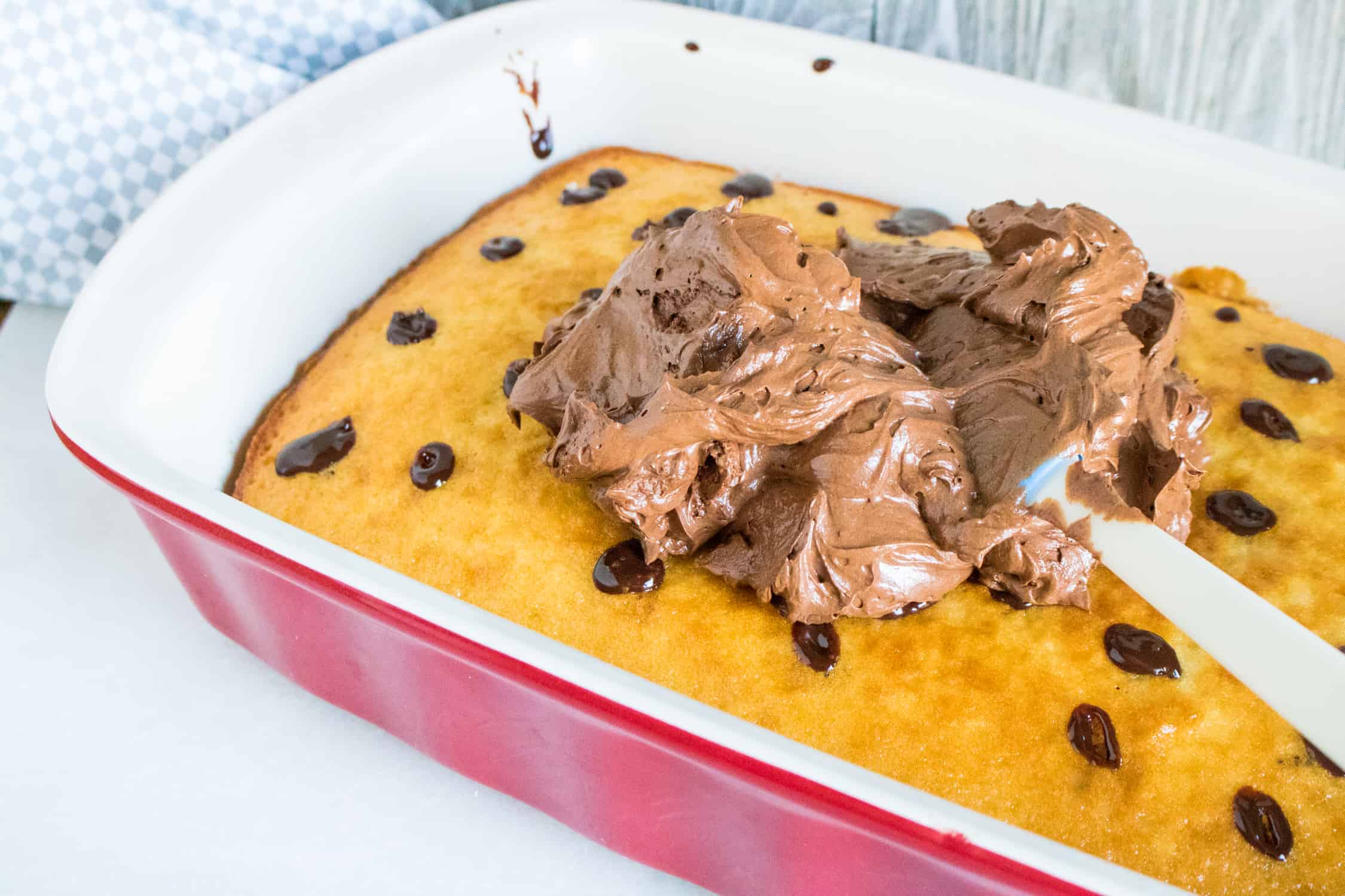 chocolate ganache whipped topping being spread onto the cooled poke cake