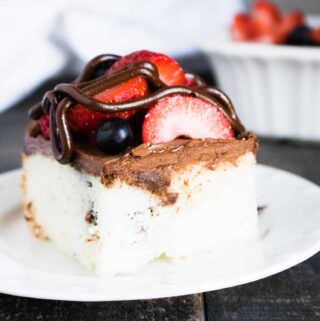 Chocolate Ganache Poke Cake with Berries sliced and served on a white dessert plate