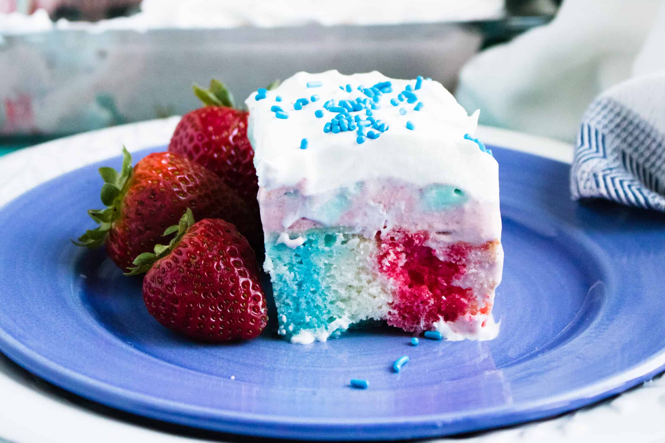 One slice of 4th of July Poke Cake with Frozen Strawberry Layer served on a blue plate and garnished with three strawberries
