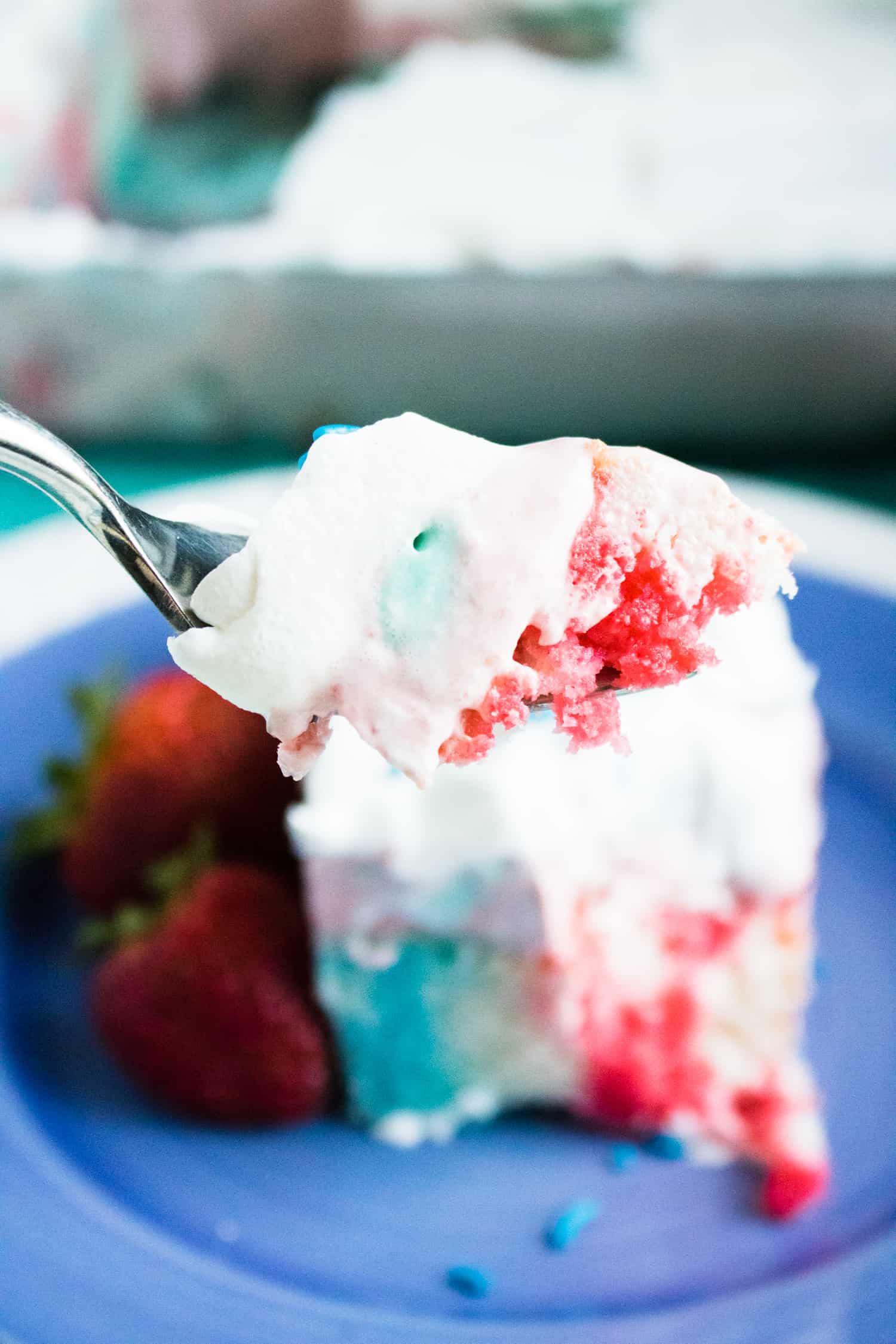 Close-up view of a forkful of 4th of July Poke Cake with Frozen Strawberry Layer.