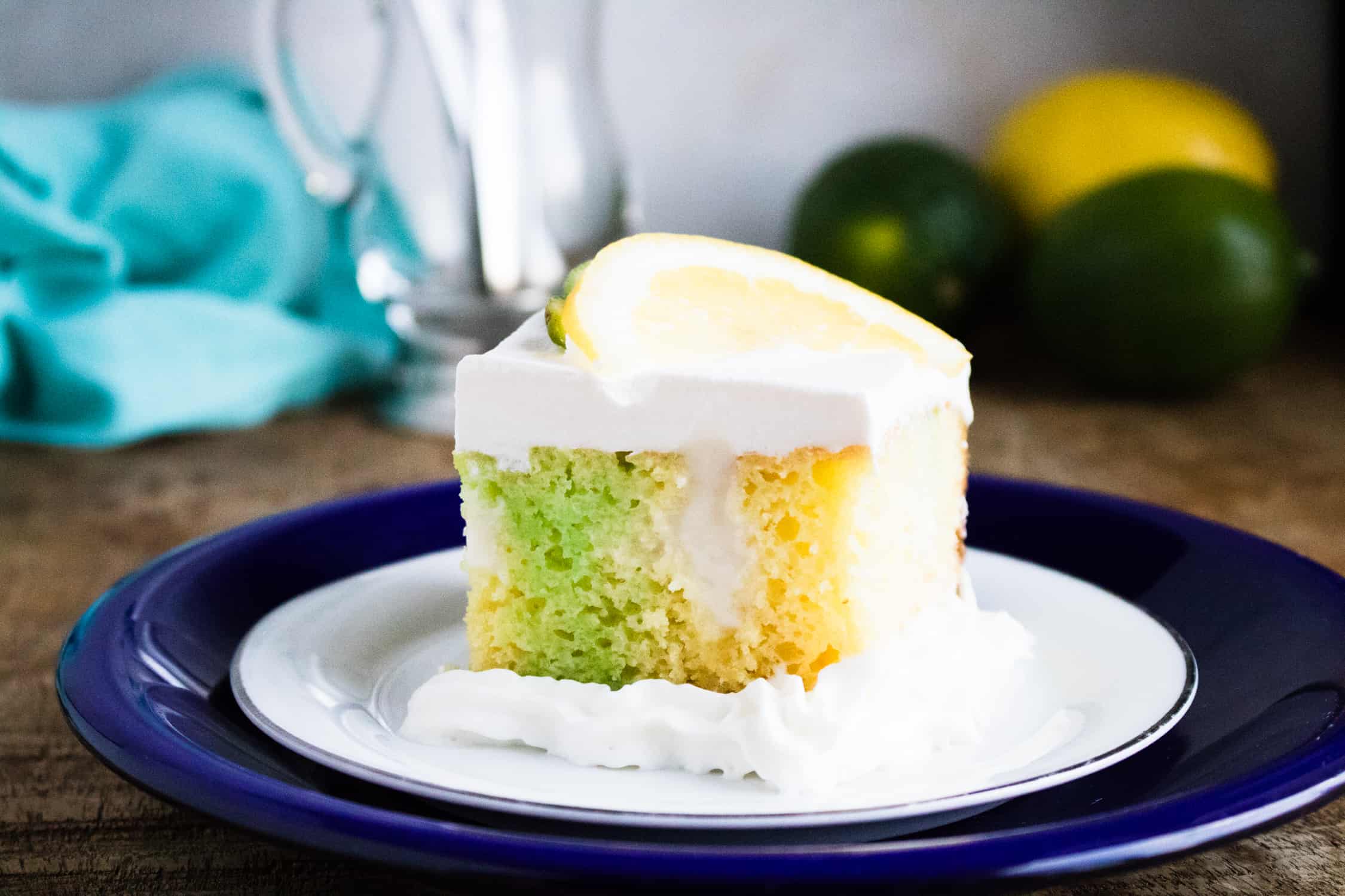 a slice of Lemon Lime Poke Cake on a white saucer on top of a blue plate