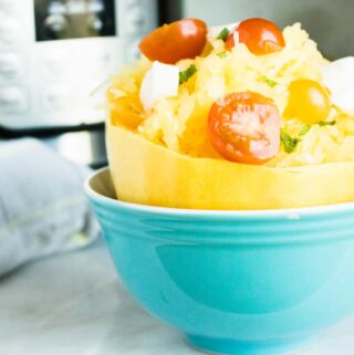 Completed Instant Pot Spaghetti Squash served in a blue bowl and topped with sliced sherry tomatoes and crumbled cheese