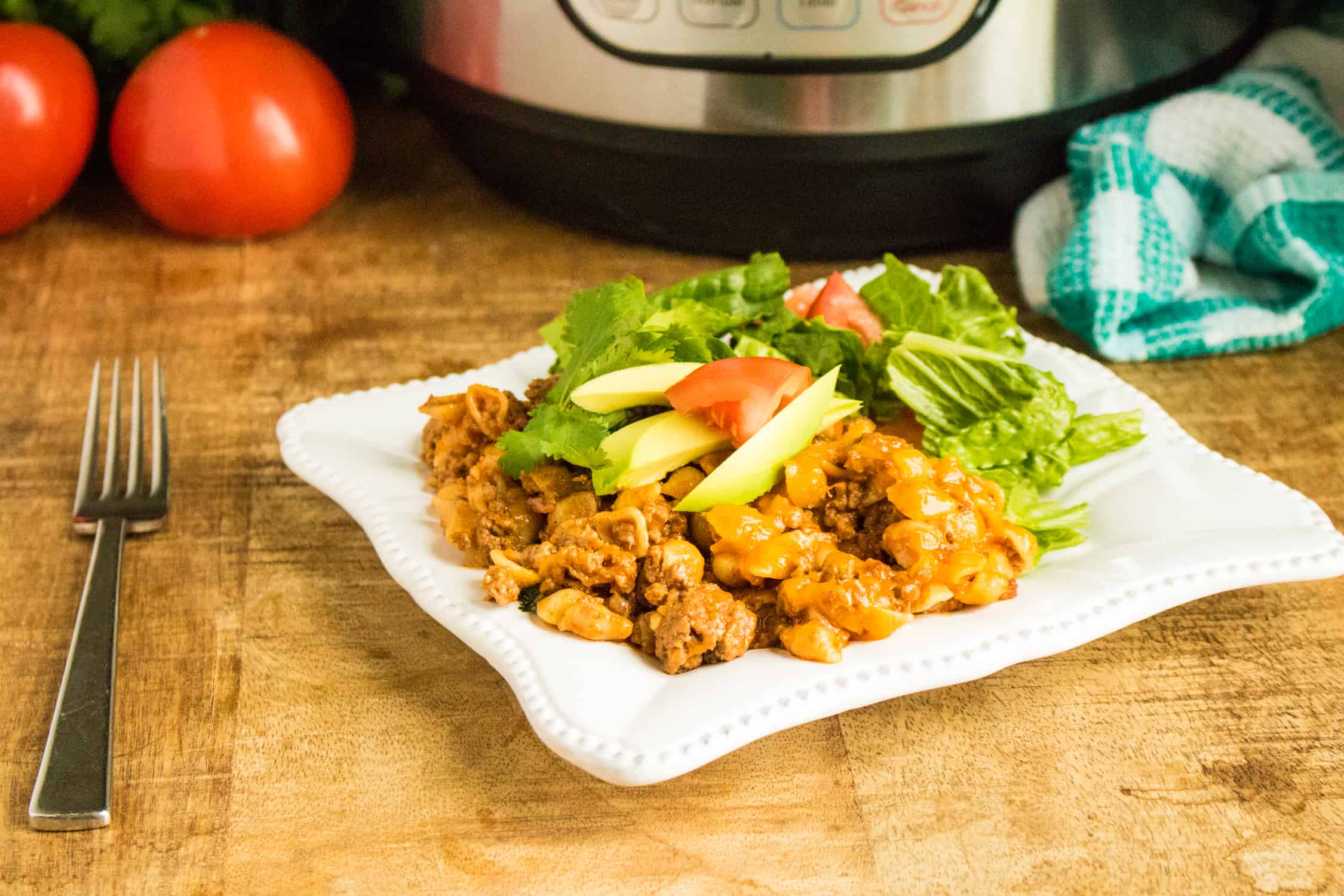 Instant Pot Taco Pasta is ready for Taco Tuesday served on a white plate and topped with tomato, lettuce, and avocado