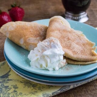 Snickerdoodle Crepes served on a blue plate next to a yellow print napkin and silver spoon