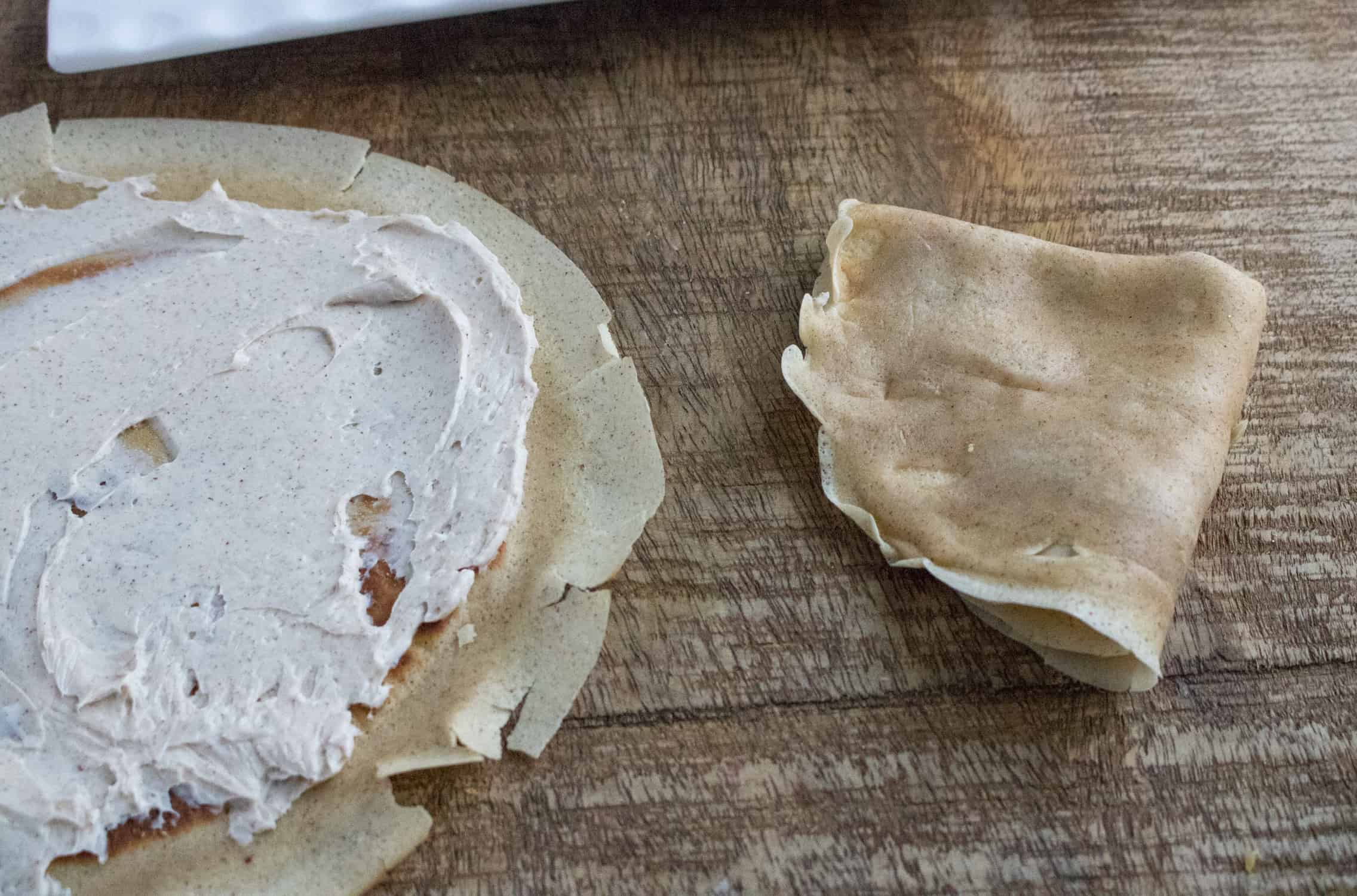 one folded crepe and one flat crepe with cream cheese filling spread on it sitting on a wood table top