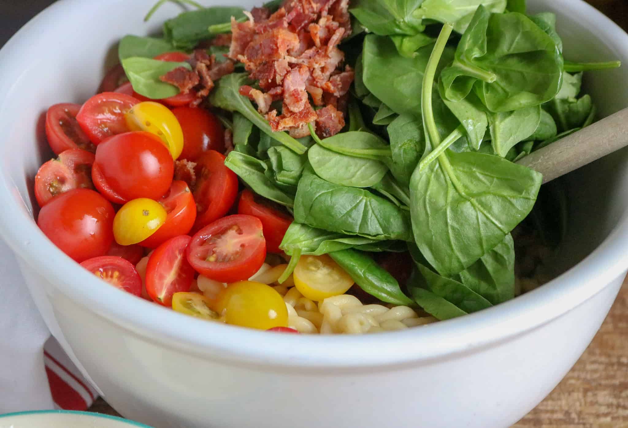 BLT Pasta Salad ingredients cherry tomatoes, spinach, bacon, yellow tomatoes and pasta in white ceramic bowl