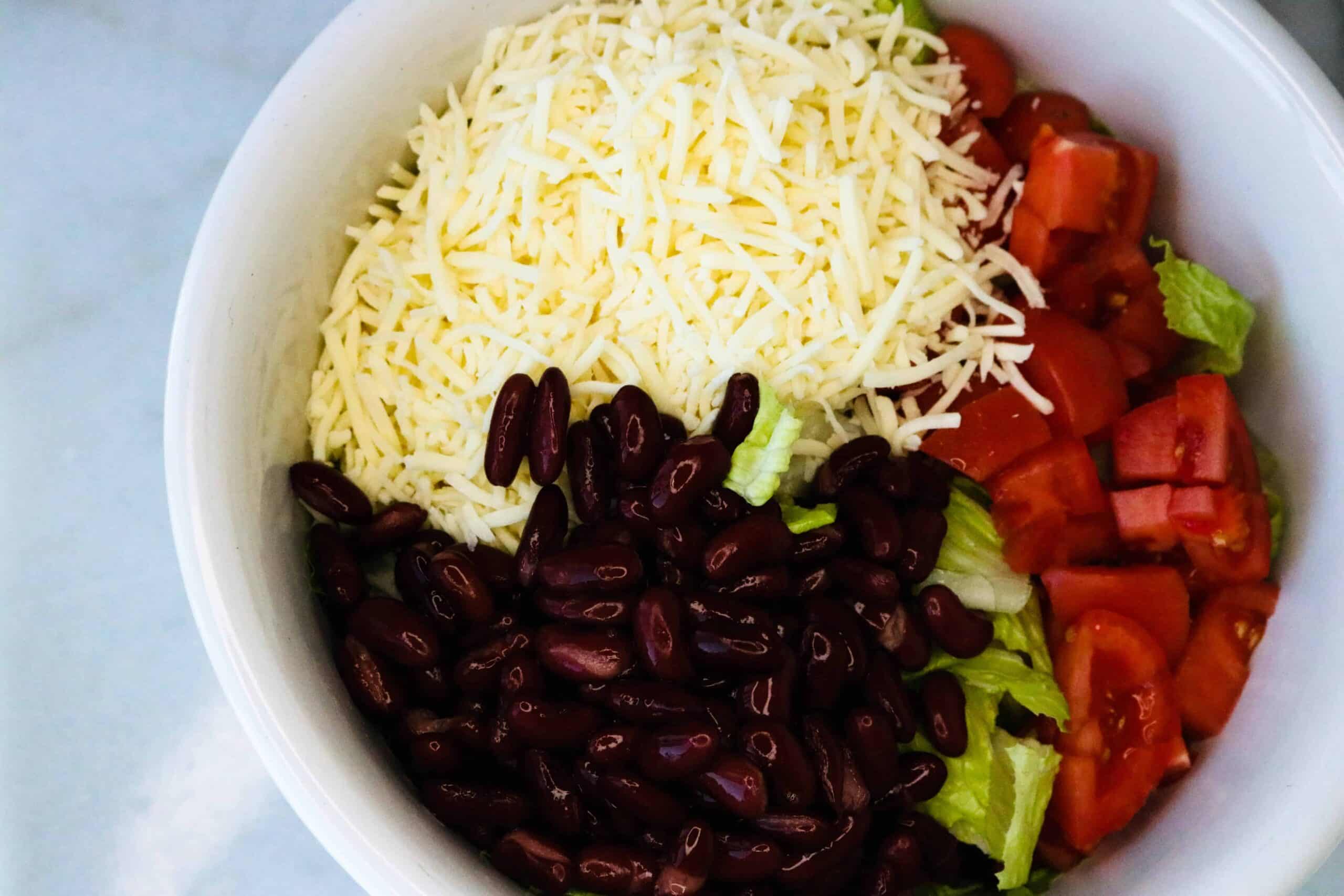Monterrey Jack cheese, sliced tomatoes, kidney beans and lettuce in a white bowl