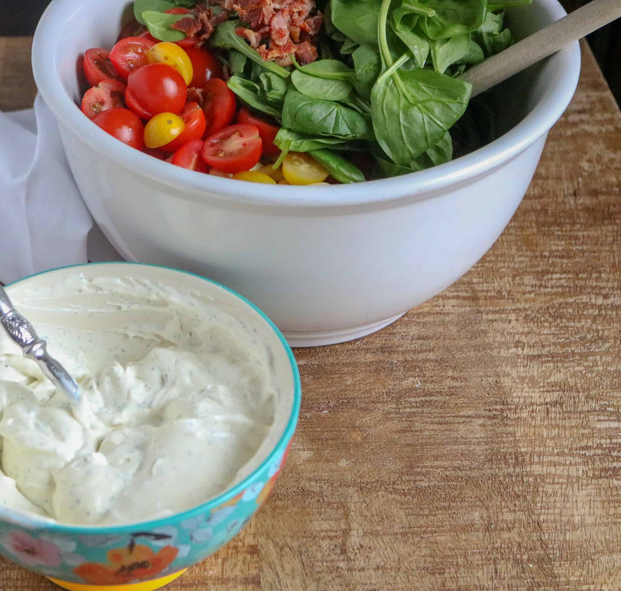 BLT Pasta Salad ingredients in white ceramic bowl in background. Mayonnaise/dressing mix in blue floral bowl in foreground
