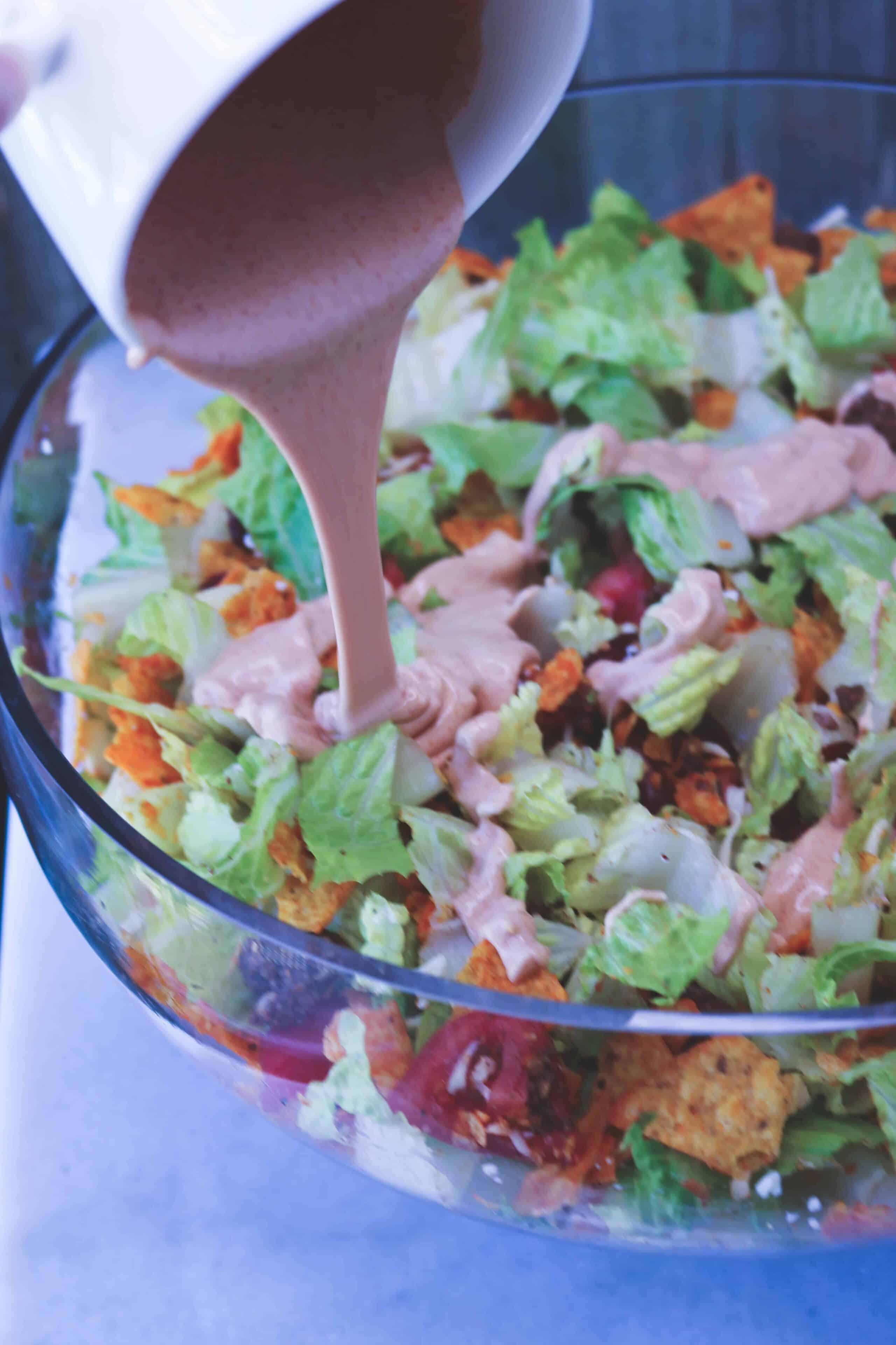 Doritos Taco Salad in a glass bowl with homemade dressing being poured over the top