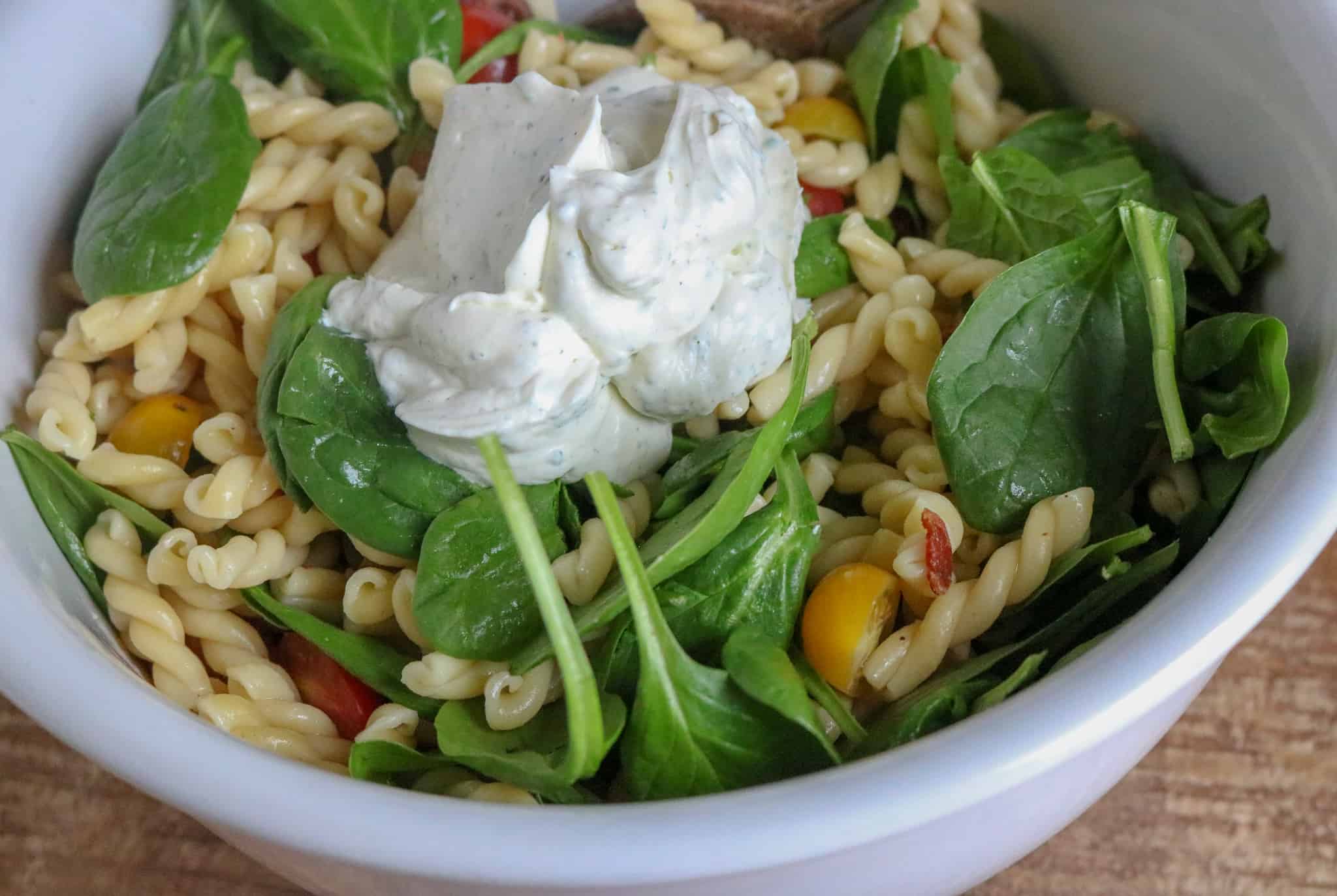 BLT pasta salad ingredients in a white mixing bowl with dressing being added