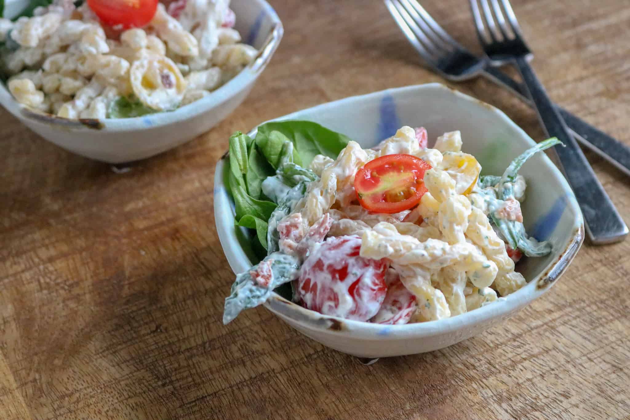 two portions of Delicious BLT Pasta Salad served in white bowls placed next to a pair of forks