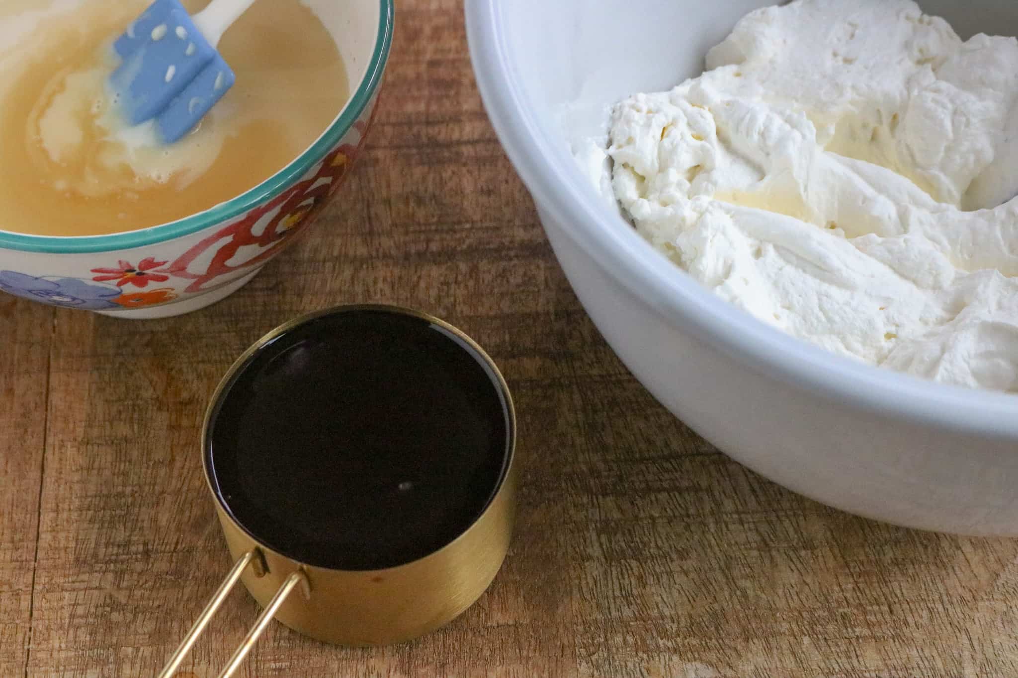 Bowl with whipped cream, bowl with sweetened condensed milk and measuring cup with chocolate syrup.