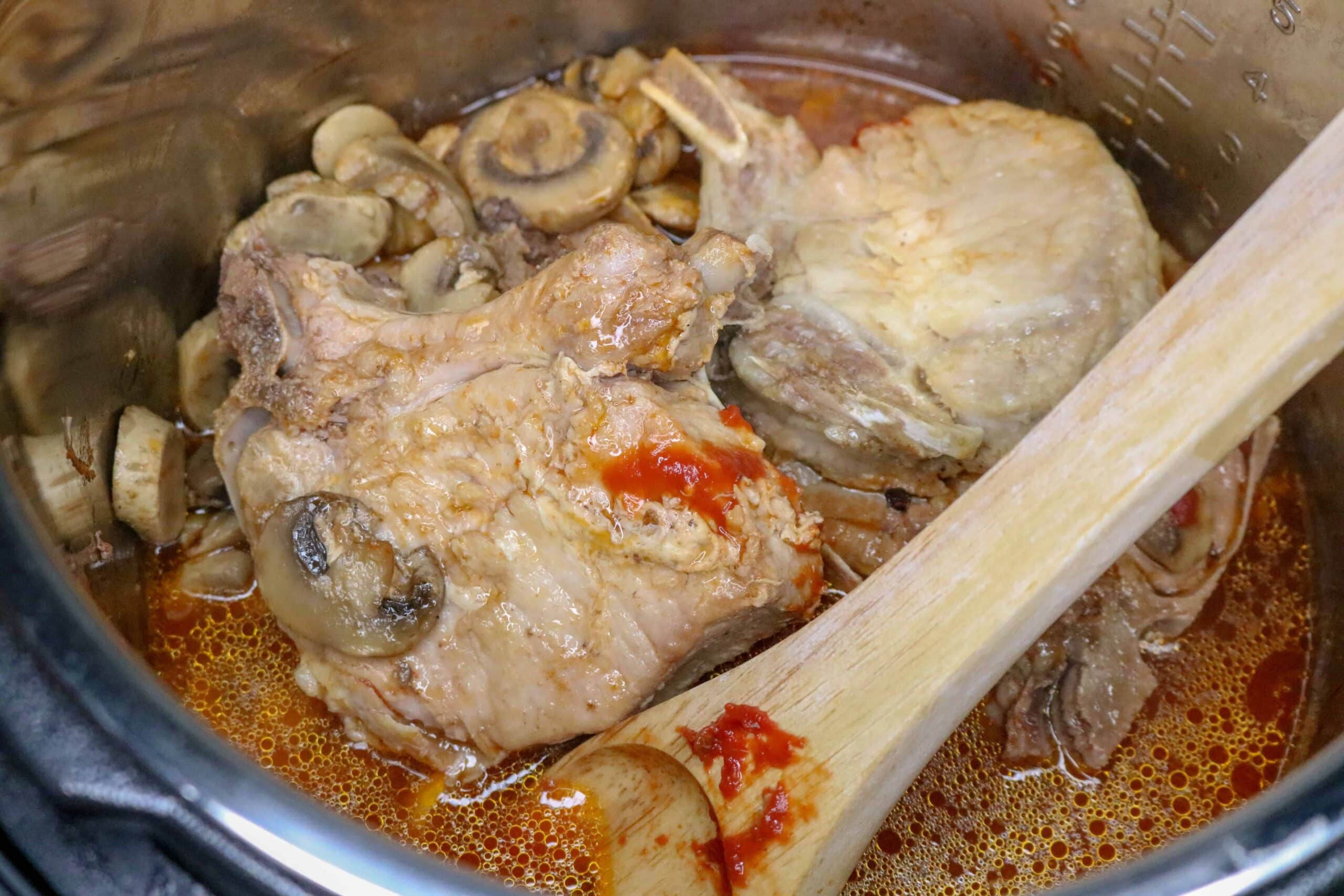 cooked pork chops in tomato cream sauce and mushrooms being stirred by wooden spoon