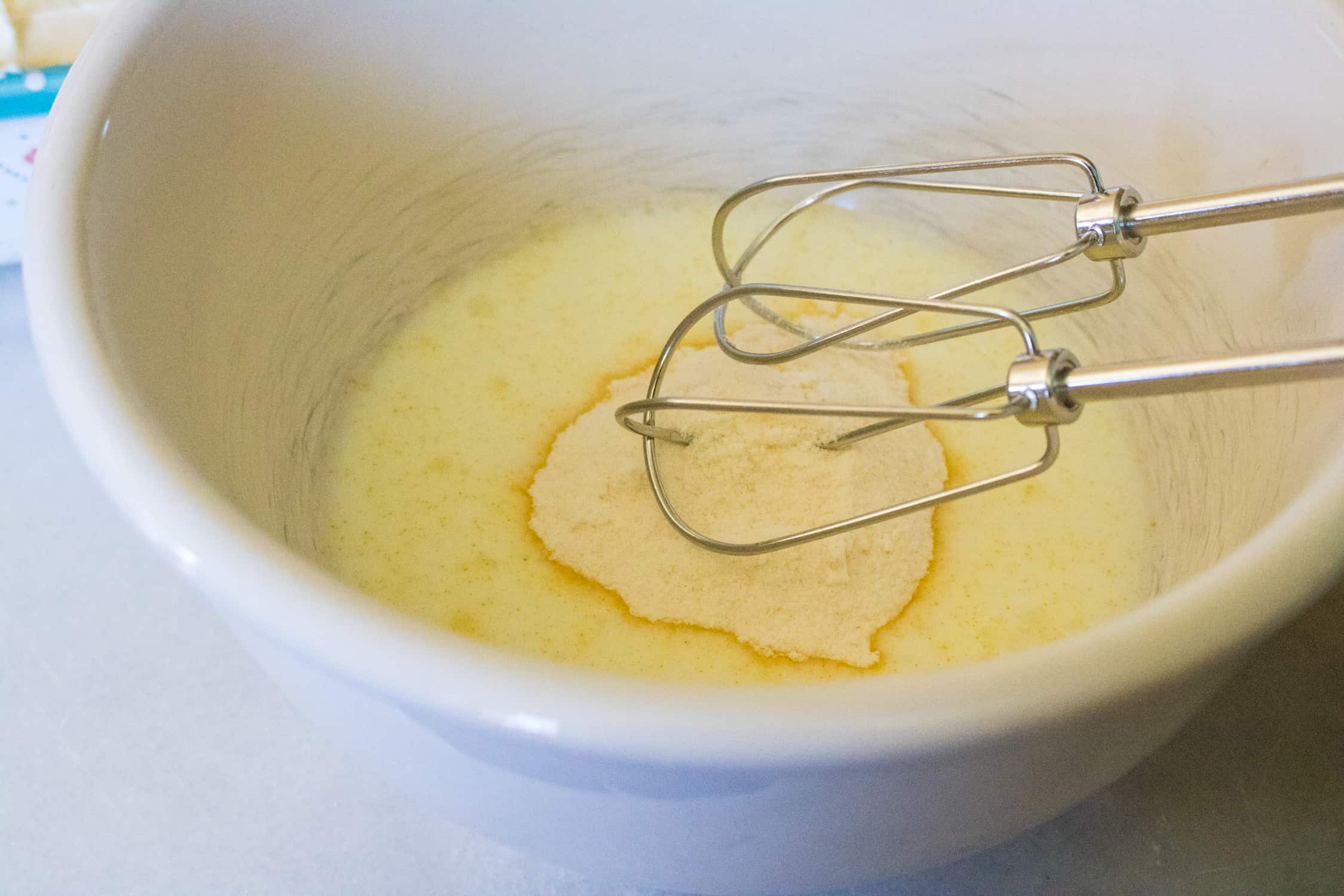 Close up view of a white bowl containing the orange cream cheese filling ingredients being mixed with an electric beater
