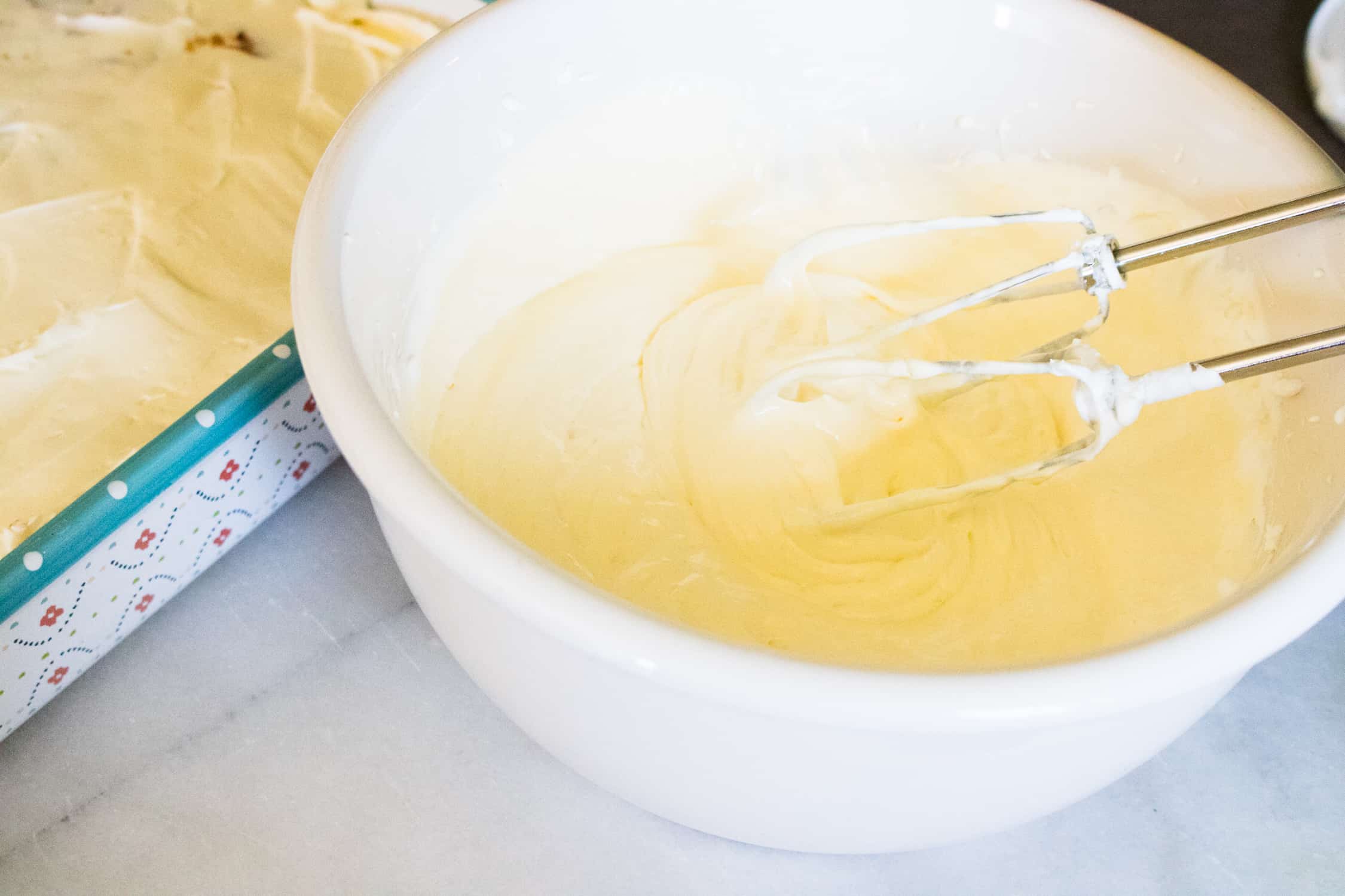 Close up view of a white bowl containing the banana pudding ingredients being mixed with an electric beater