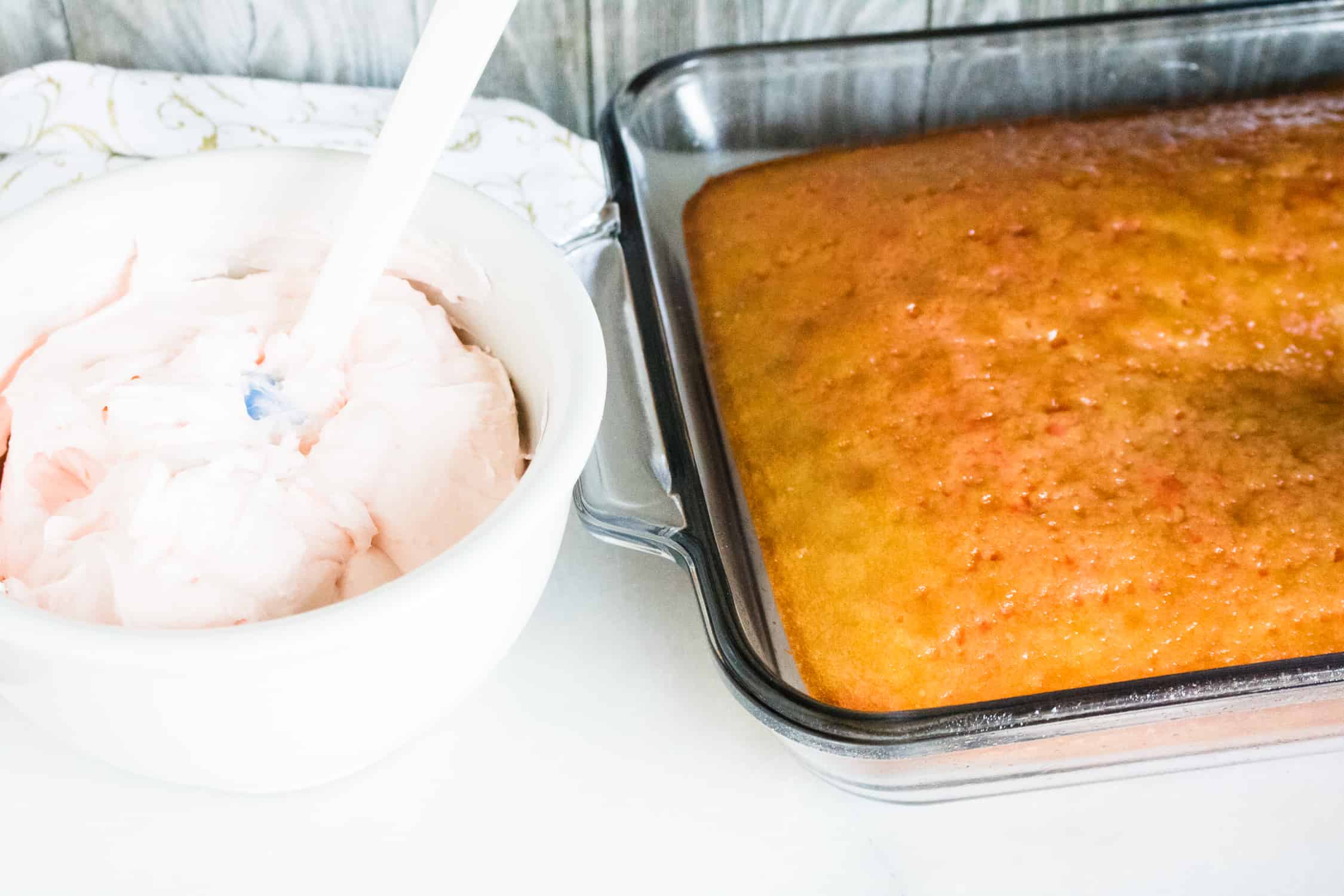 close up view of the poke cake next to a white mixing bowl containing the blended cream cheese mixture