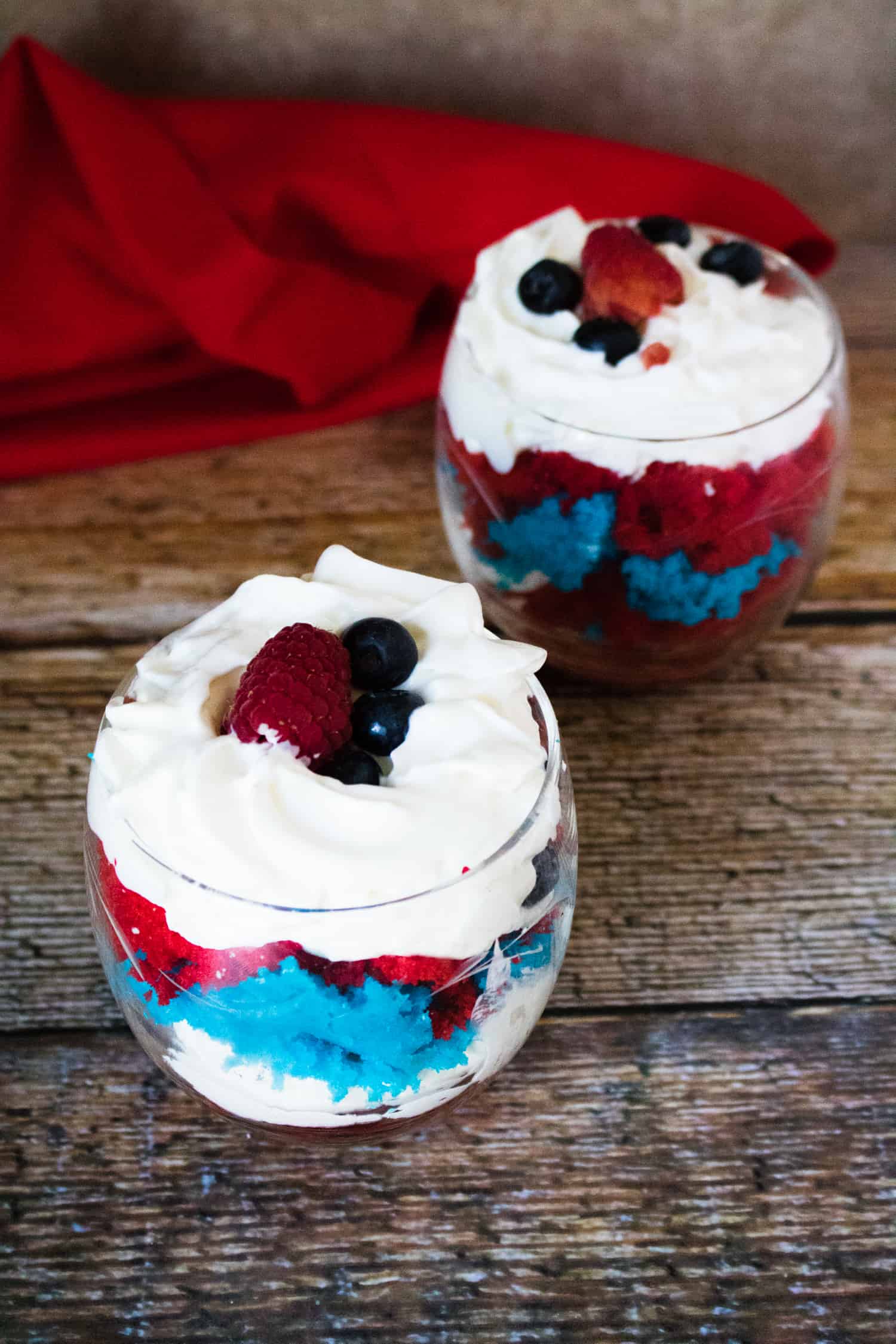 top-down view of two of these 4th of July Desserts served in glass dessert cups sitting in front of a red cloth napkin
