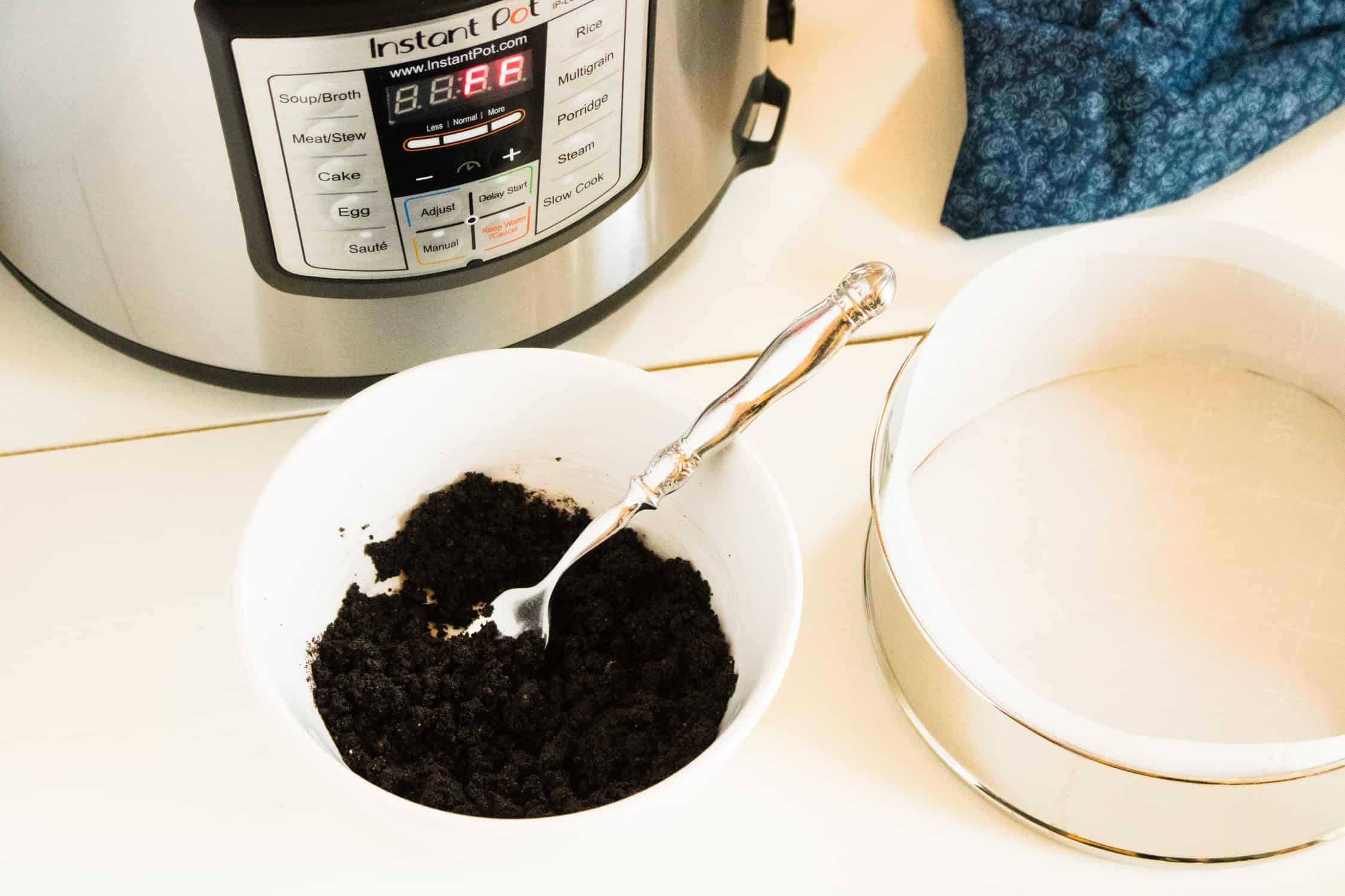 oreo cookie crumbs in a white bowl on a table next to a springform pan and an Instant Pot