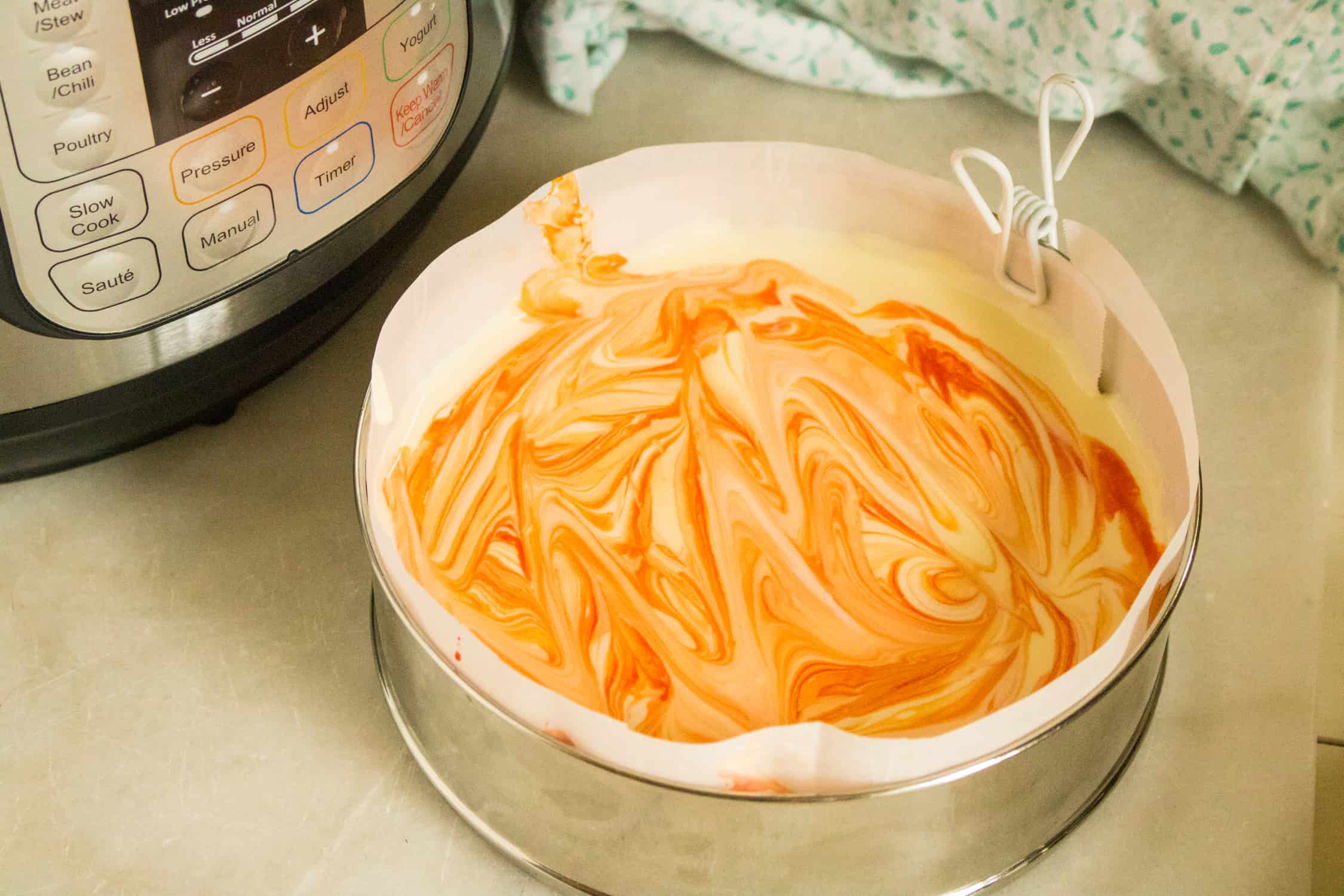 spring form pan with batter for instant pot orange creamsicle cheesecake in it that has been swirled with orange food coloring for color