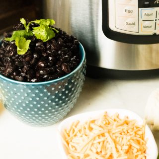 Instant Pot Black Beans served in a blue polka dot bowl set next to the instant pot and a white plate with shredded cheese