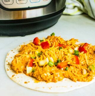 Instant Pot Buffalo Chicken served on a tortilla and garnished with diced tomato, onion and green pepper