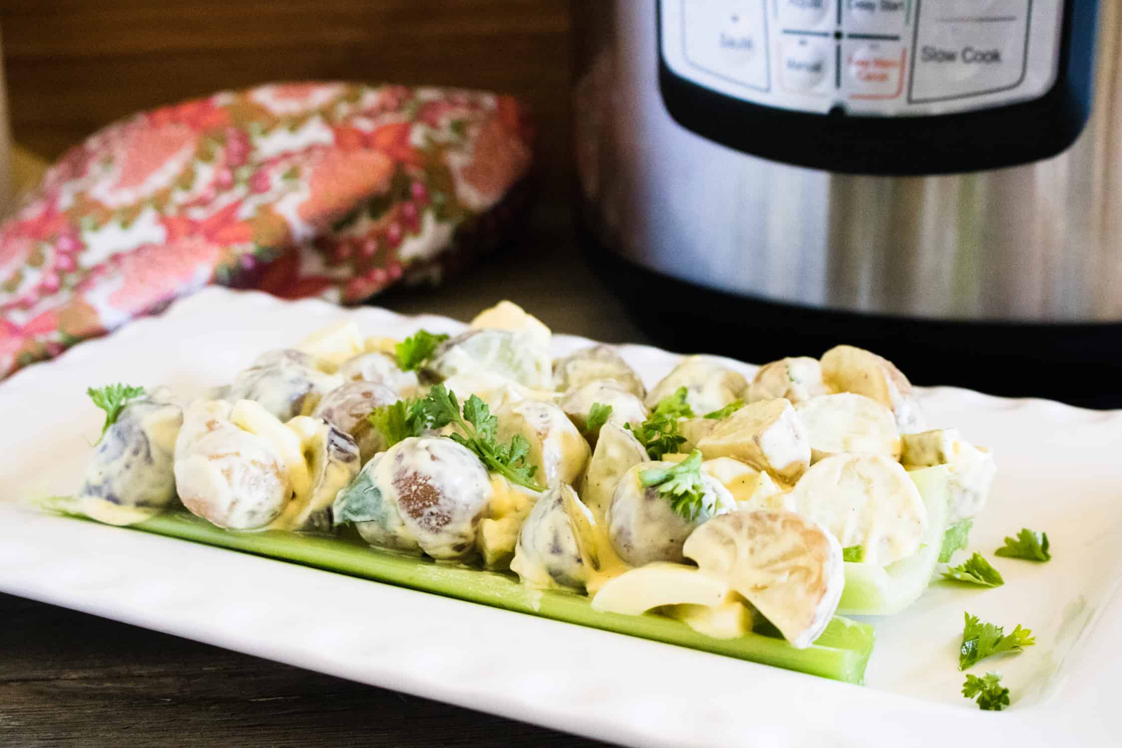 instant pot heirloom potato salad on rectangular white plate with silver instant pot and red printed towel in background