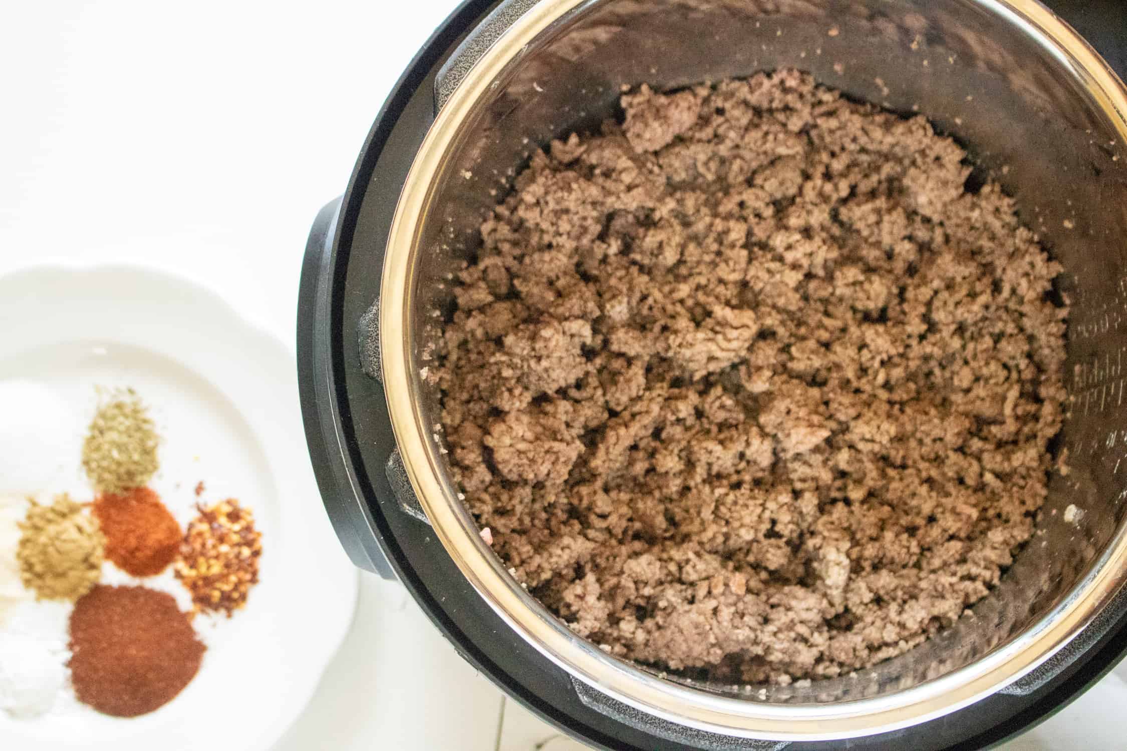 Cooked Taco Meat in an Instant Pot sitting next to a plate of spices