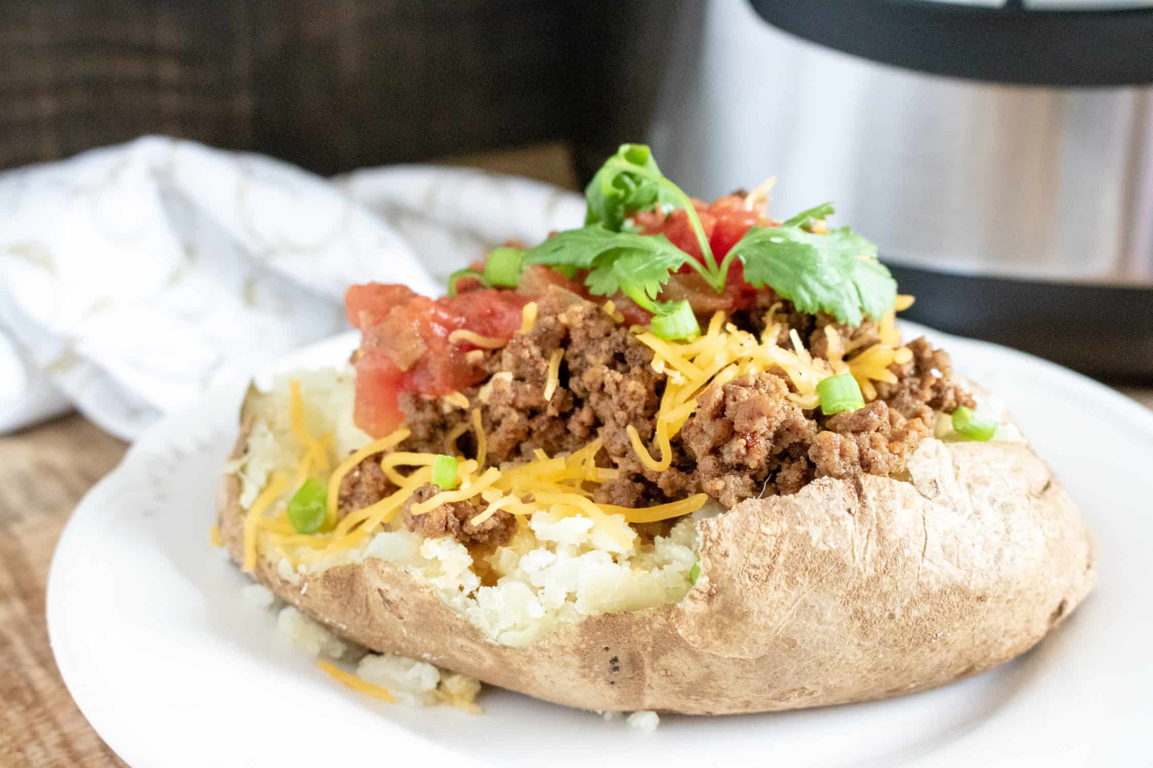Instant Pot Taco Meat on a baked potato topped with cheese, cilantro and tomatoes 