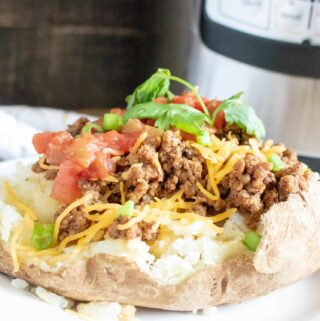 Instant Pot Taco Meat served on a baked potato and topped with cheese, tomato, and cilantro