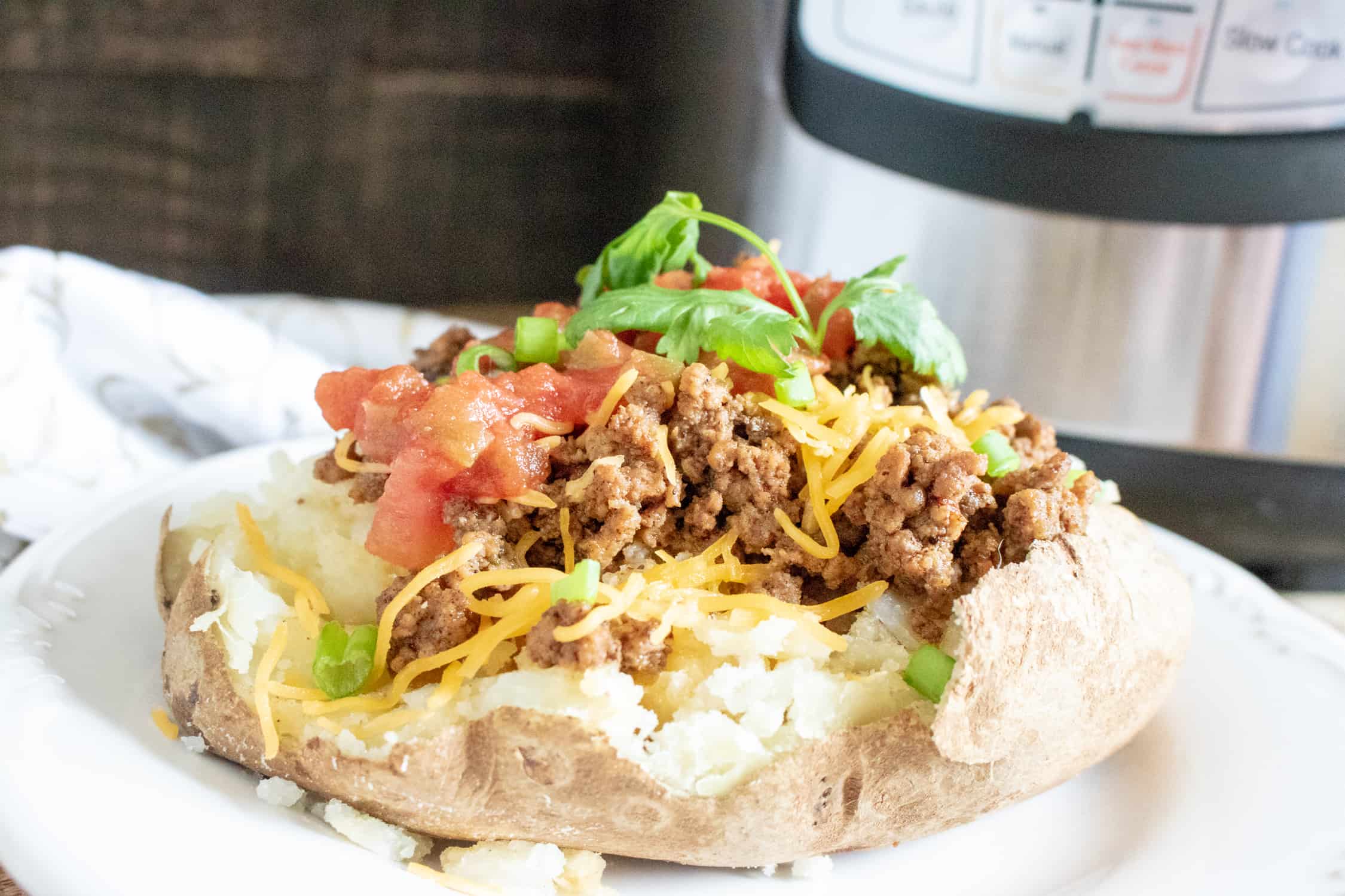 Instant Pot Taco Meat on a baked potato topped with cheese, cilantro and tomatoes 